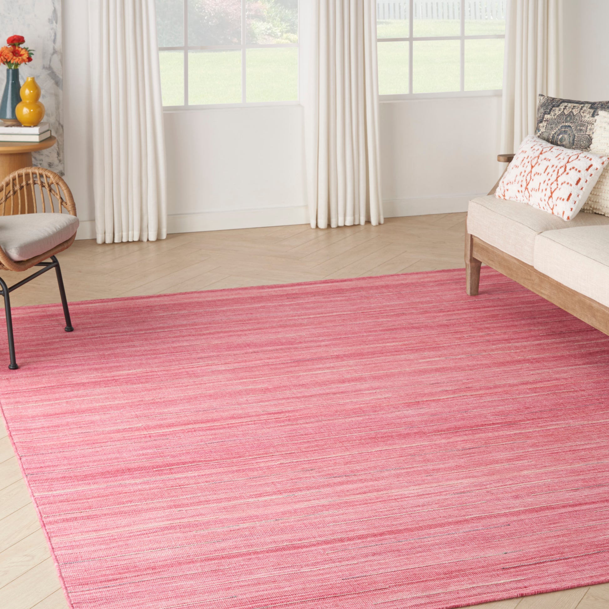 Rectangular pink striped area rug on light wood floor in a bright living room with cream curtains and sofa.