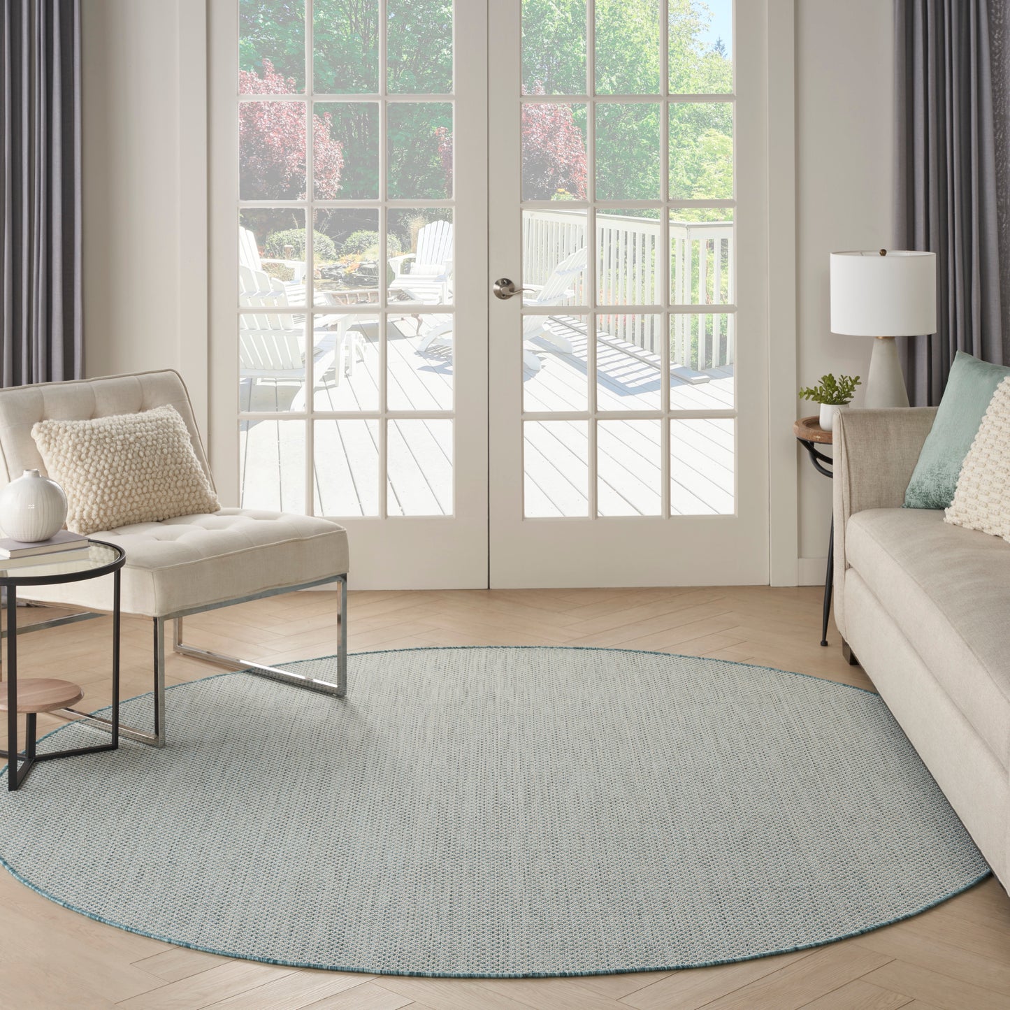 Light blue round rug on a pale wood floor in a modern living room with a beige sofa and glass French doors.