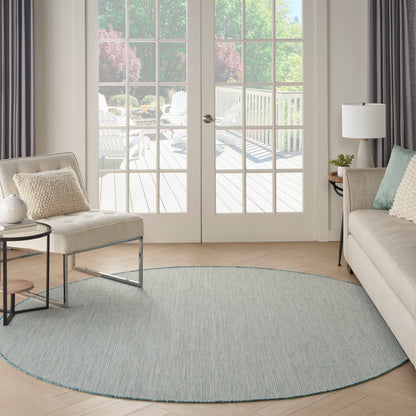 Light blue round rug on a pale wood floor in a modern living room with a beige sofa and glass French doors.