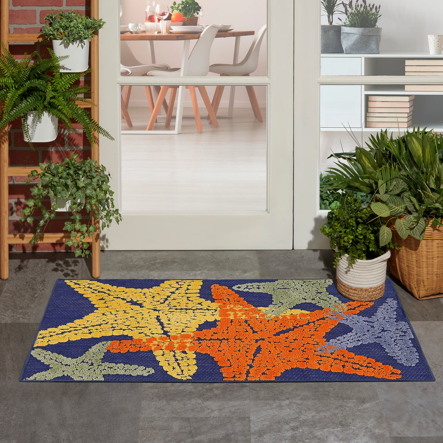 Coastal outdoor entry doormat featuring large yellow and orange starfish on blue, flanked by potted plants.