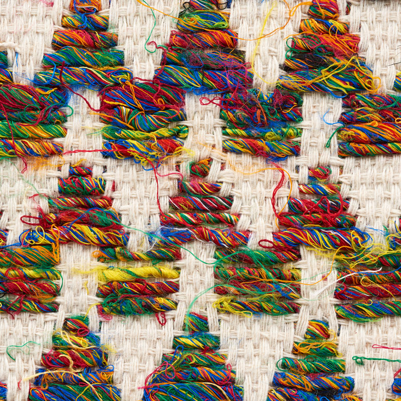 Close-up of bright rainbow yarn woven in chevron stripes on beige woven fabric.