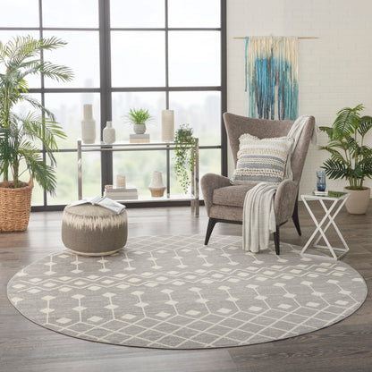 Round gray area rug with white lattice pattern in a modern sunlit living room with a gray armchair and pouf.