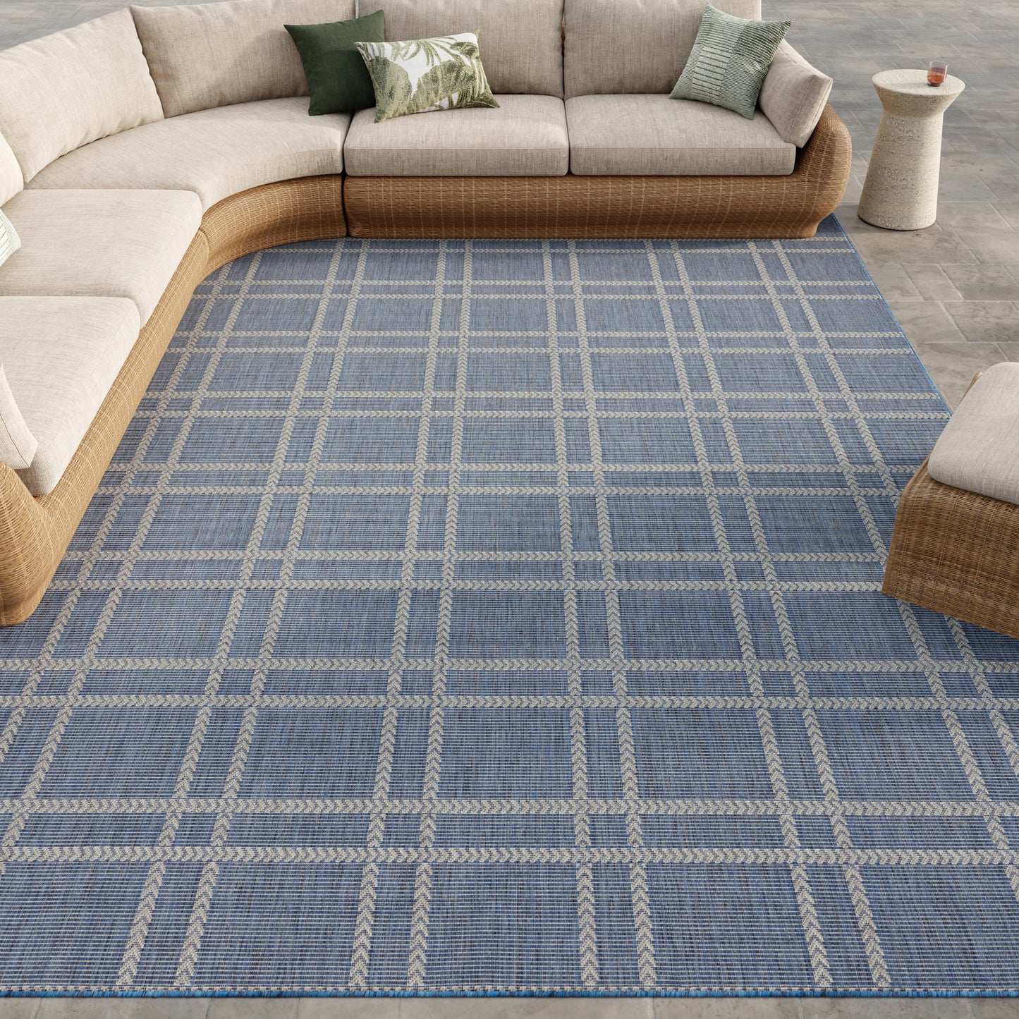 Blue plaid area rug with light beige grid lines under a beige sectional with woven rattan base in a modern living room.