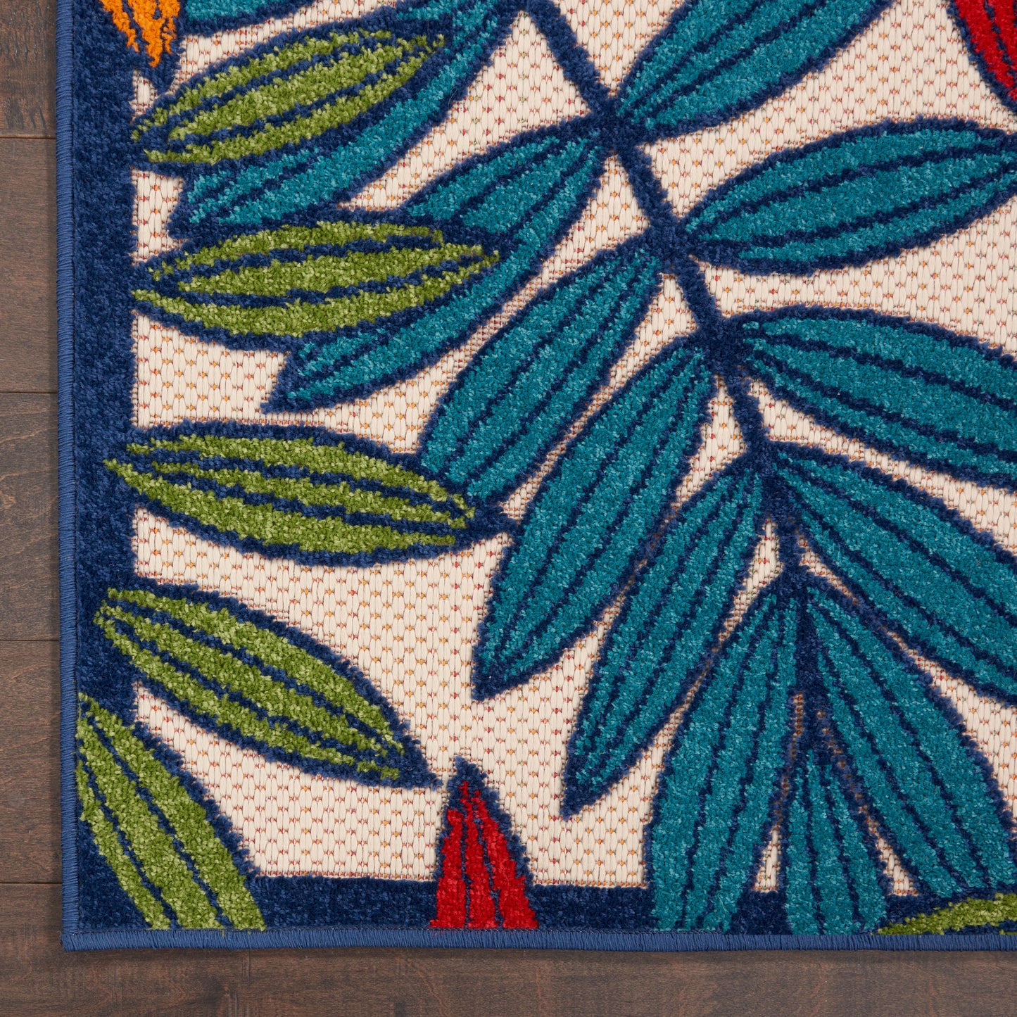 Tropical leaf-pattern rug with a dark blue border, green palm leaves & red accent on wooden floor.