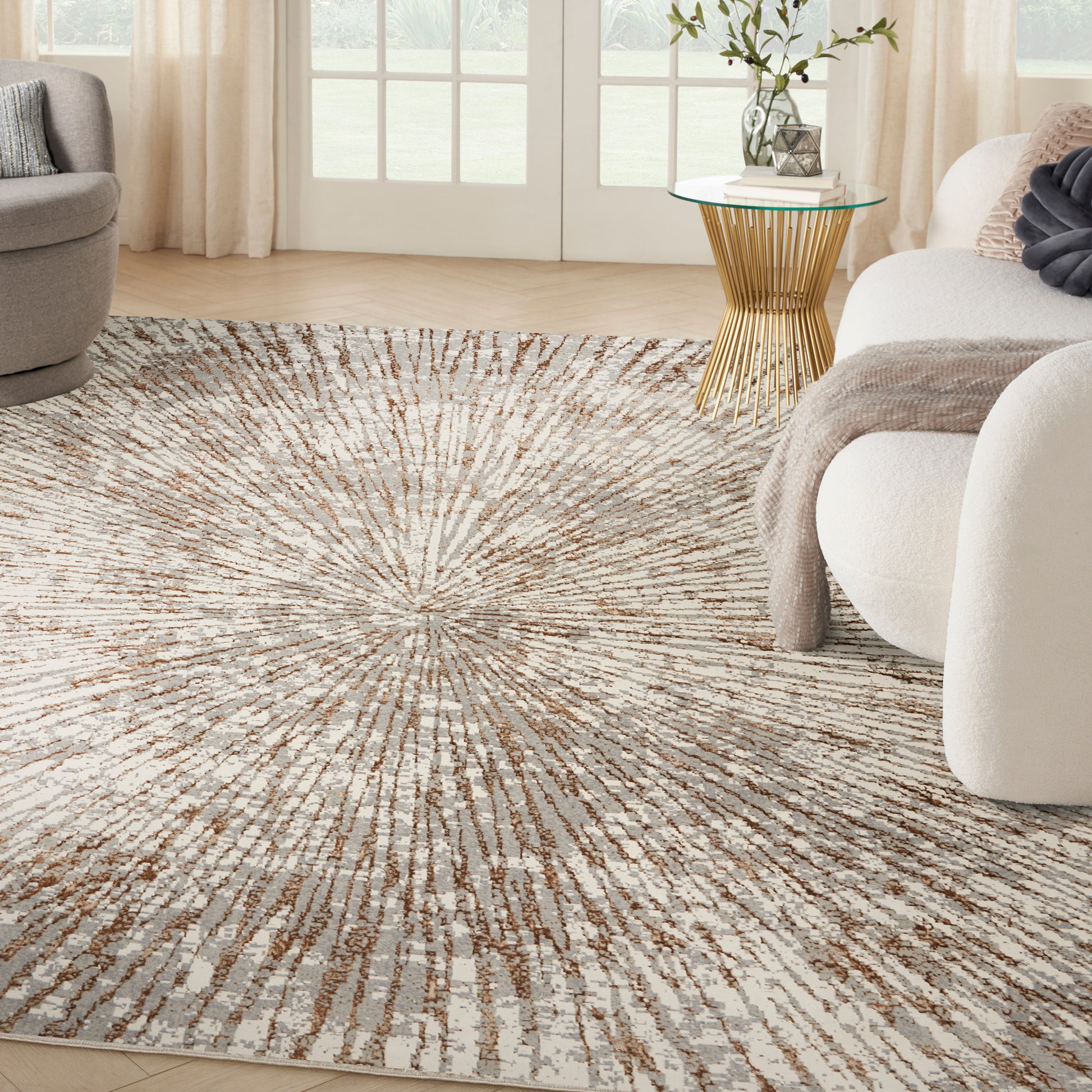 Plush beige cream sunburst area rug in a bright living room with gold glass-top side table and neutral seating.