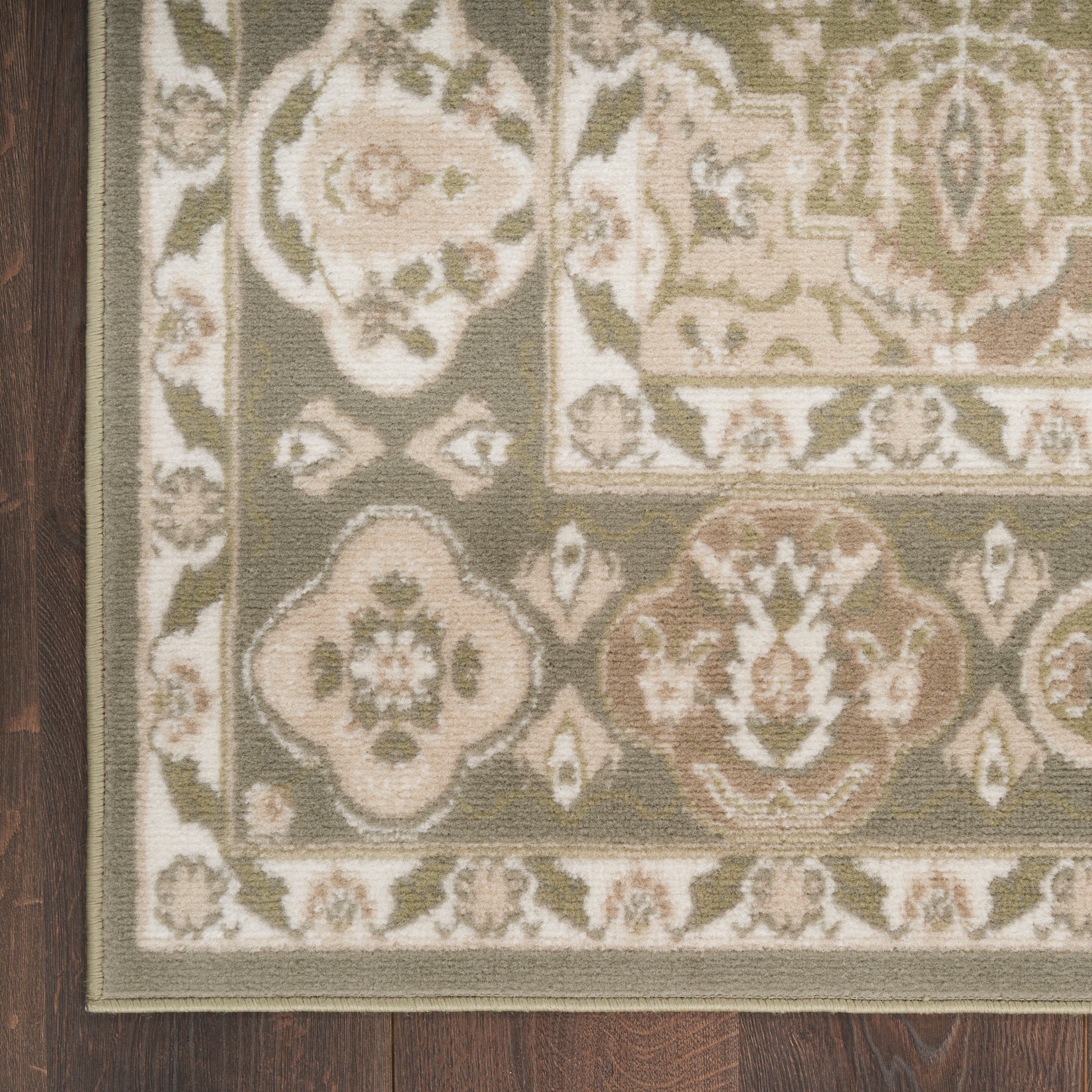 Traditional oriental area rug with floral medallions in olive, beige and cream on dark wood floor (corner view).