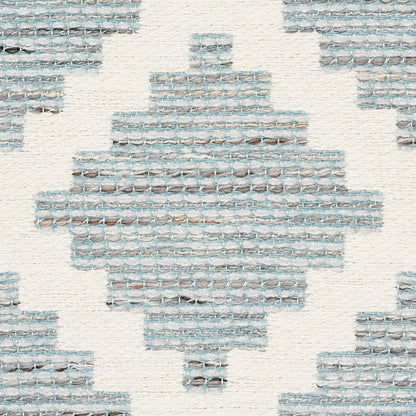 Woven rug with blue-gray geometric diamond motif on cream background; textured kilim-style textile.