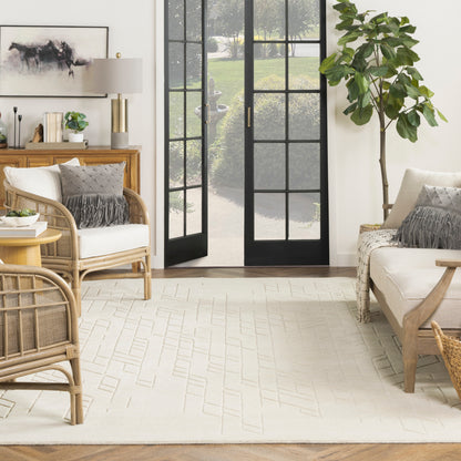 Beige geometric rug, 10' x 14', in a bright living room with rattan seating, cream cushions, black-framed French doors, and a tall potted plant.