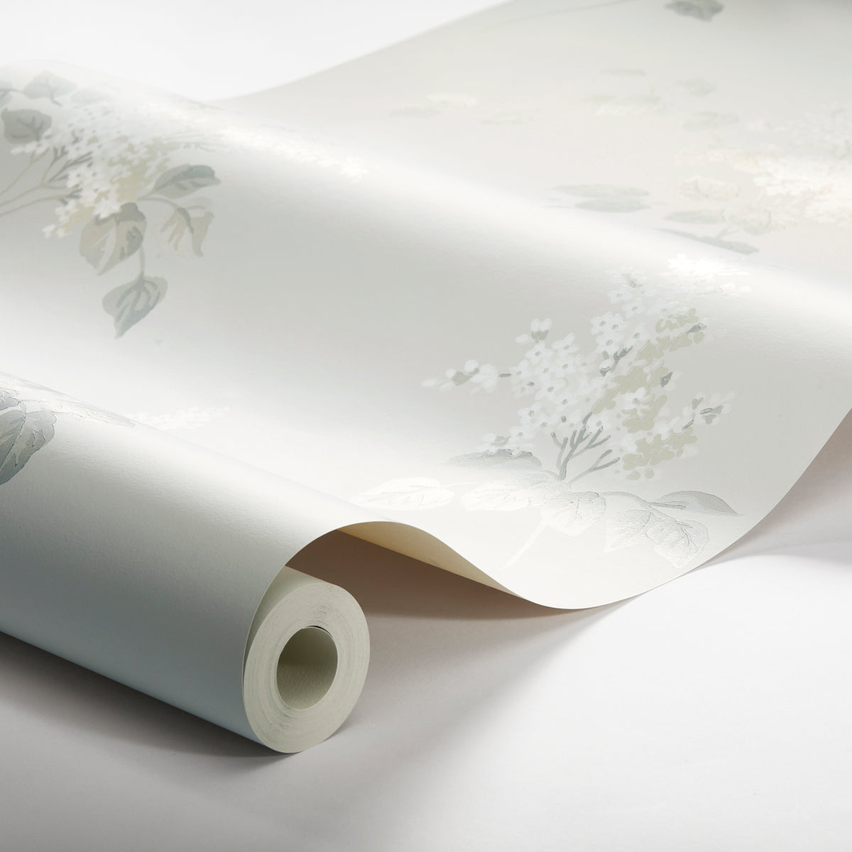 Rolled pale blue wallpaper with soft white floral botanical pattern, partially unrolled to show delicate leaves and flowers.