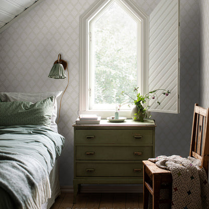 Bedroom with sage green chest, arch window, pale wallpaper, bed with green bedding, wooden chair, vase and books on dresser.