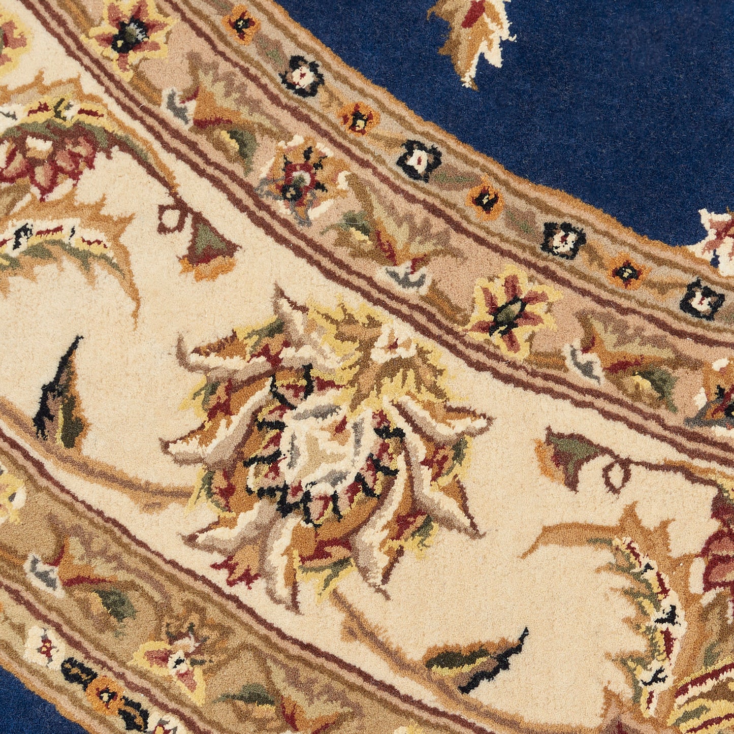 Ornate Persian-style rug with cream field, tan-gold border, multicolored floral motifs, and a deep blue accent.