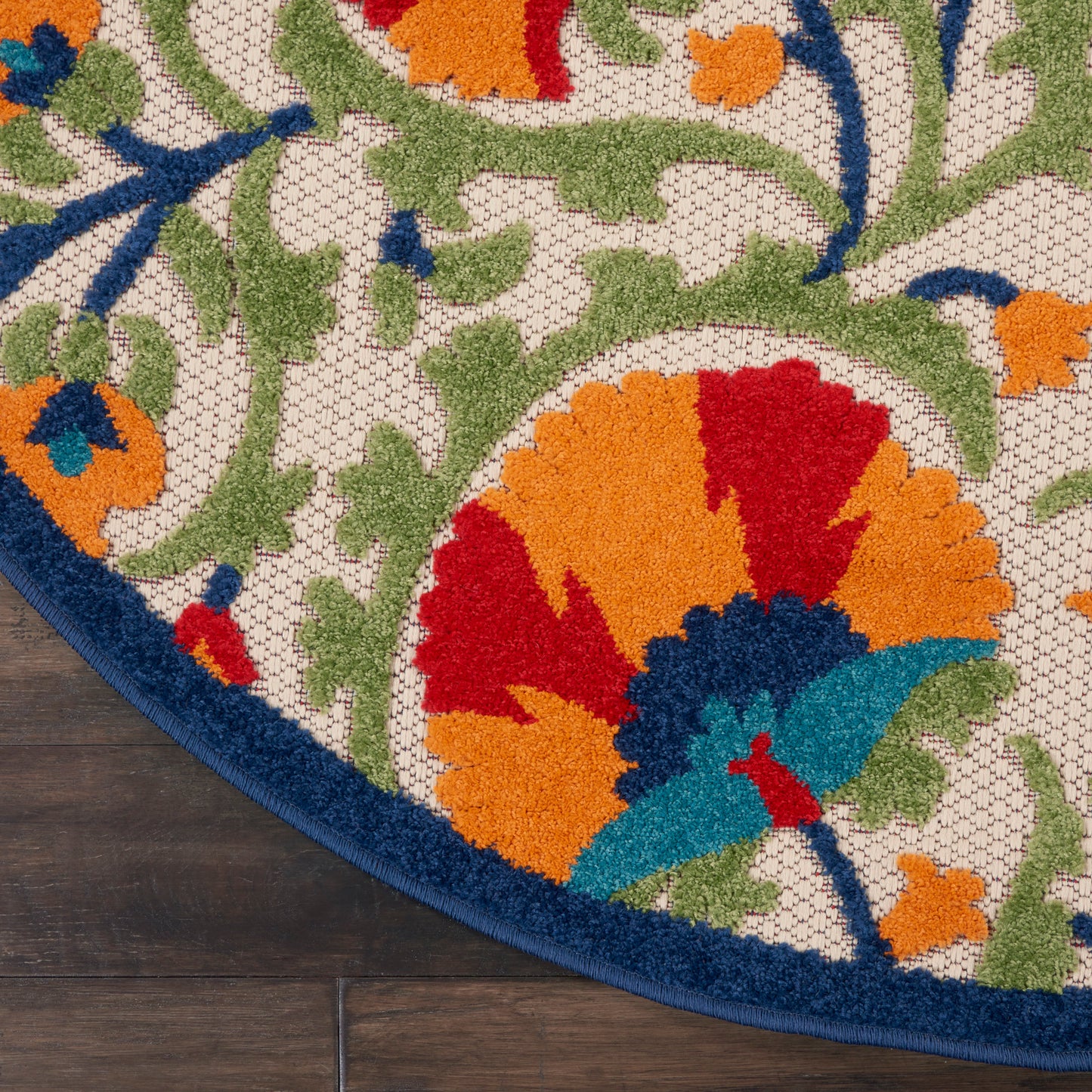 Round tufted rug with vibrant floral pattern: orange, red, teal petals, green leaves on cream lattice, navy blue border.