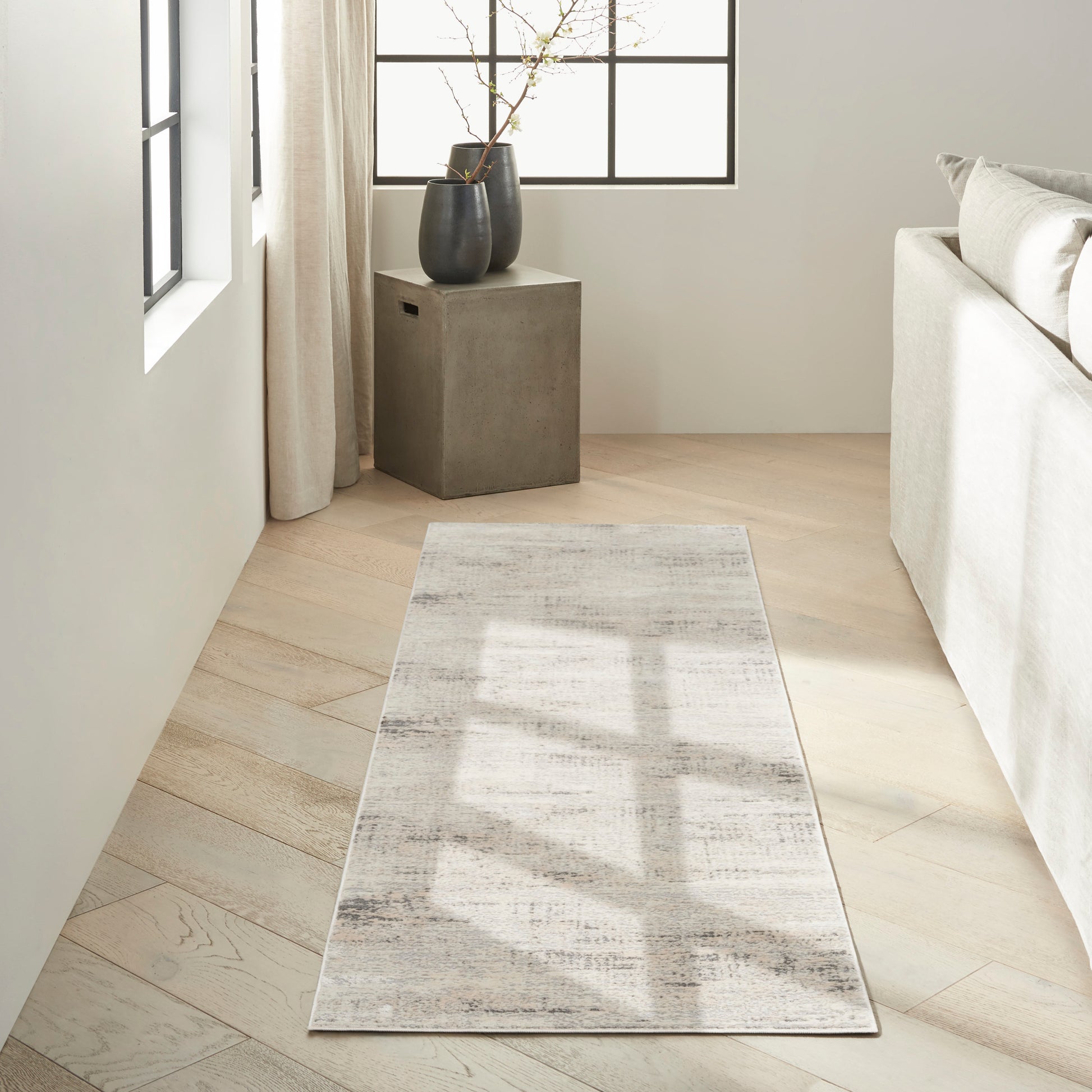 Neutral pale beige rug with subtle gray distressing on light wood floor beside a concrete side table with black vases.