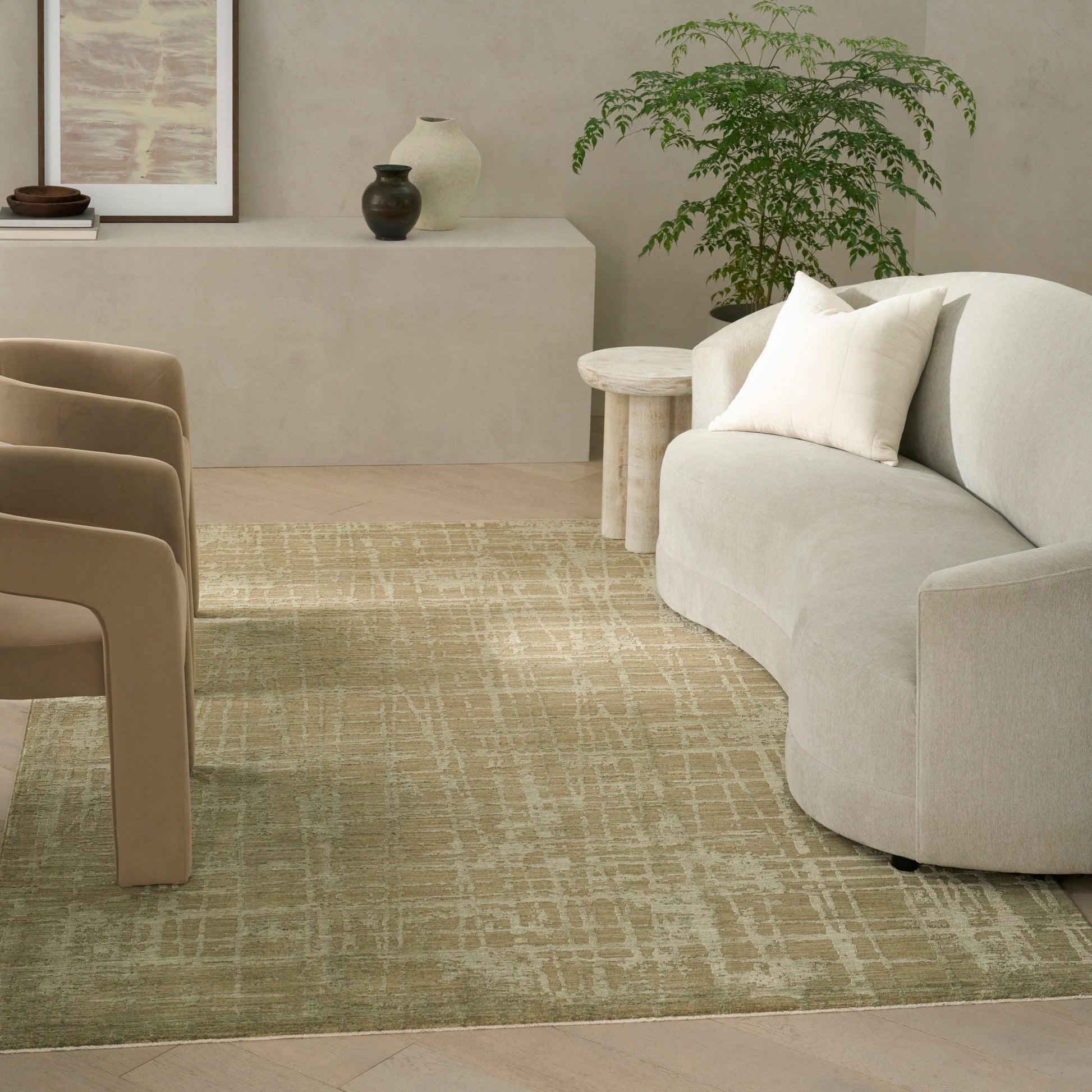 Beige curved sofa with cream cushions, round wood side tables, tan chairs, and a beige patterned rug in a serene living room.