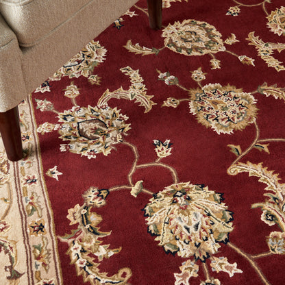 Burgundy oriental rug with large cream and gold floral motifs, bordered by a light pattern; wooden sofa leg in corner.