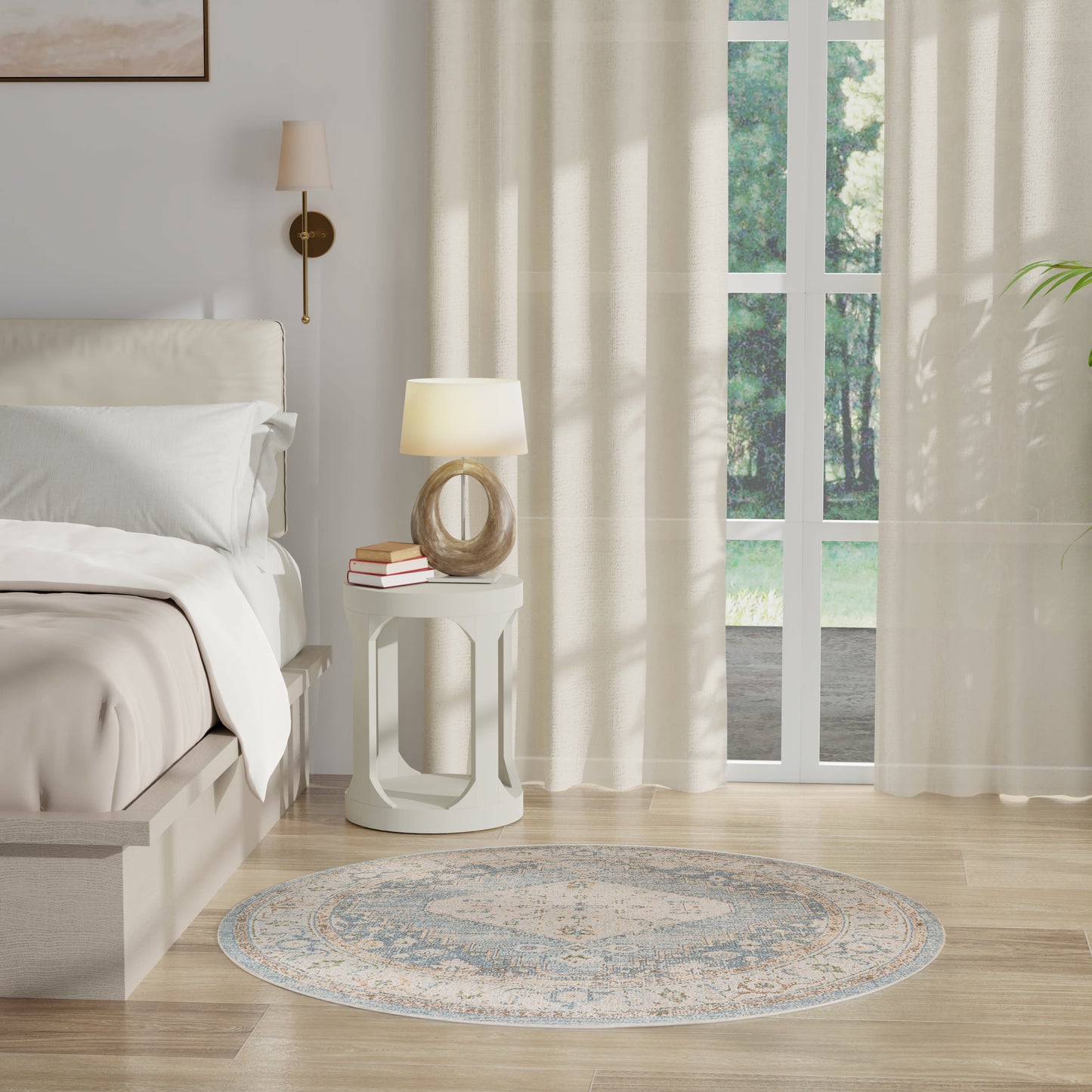 Neutral round rug in a cozy bedroom setting with white bedding, white nightstand, sheer curtains, and glass doors to a garden.