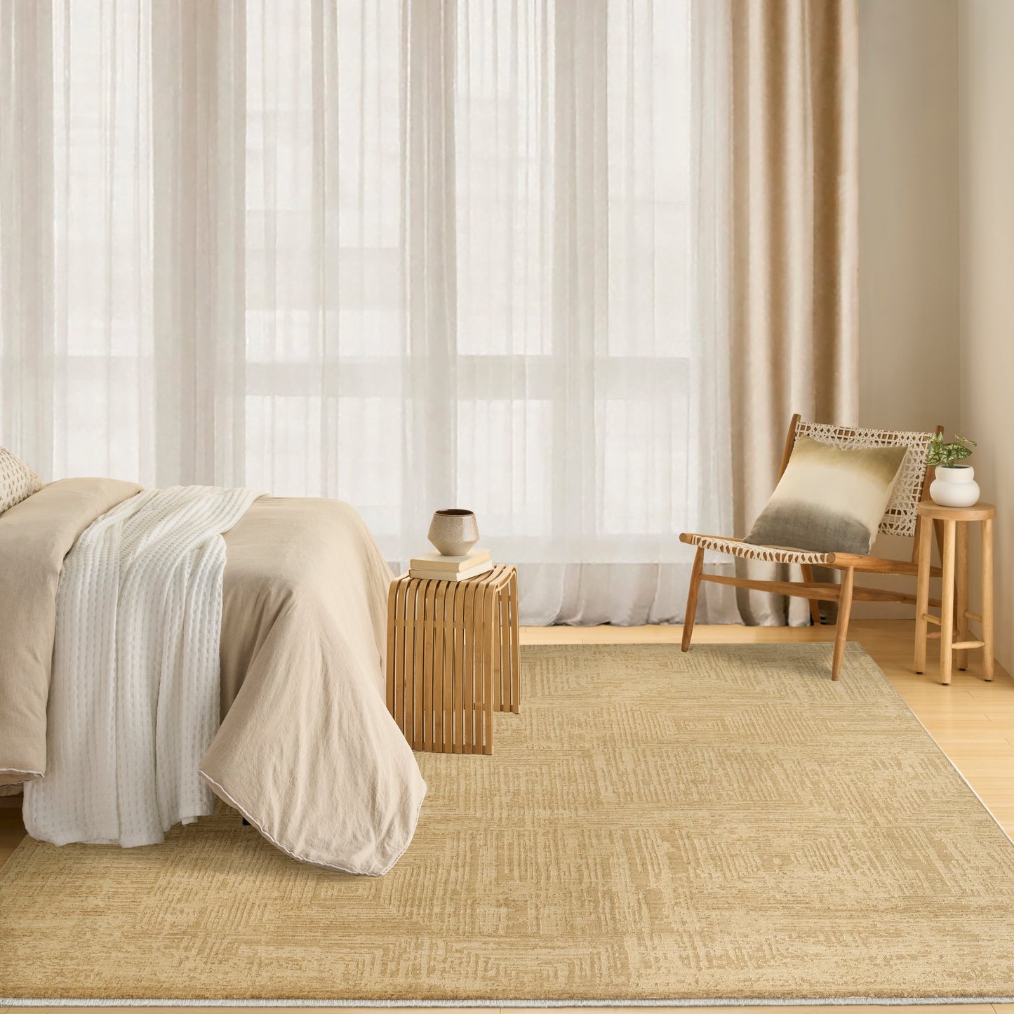 Neutral bedroom with beige linen bedding, sheer cream curtains, woven jute rug, and wooden chair with small side tables.