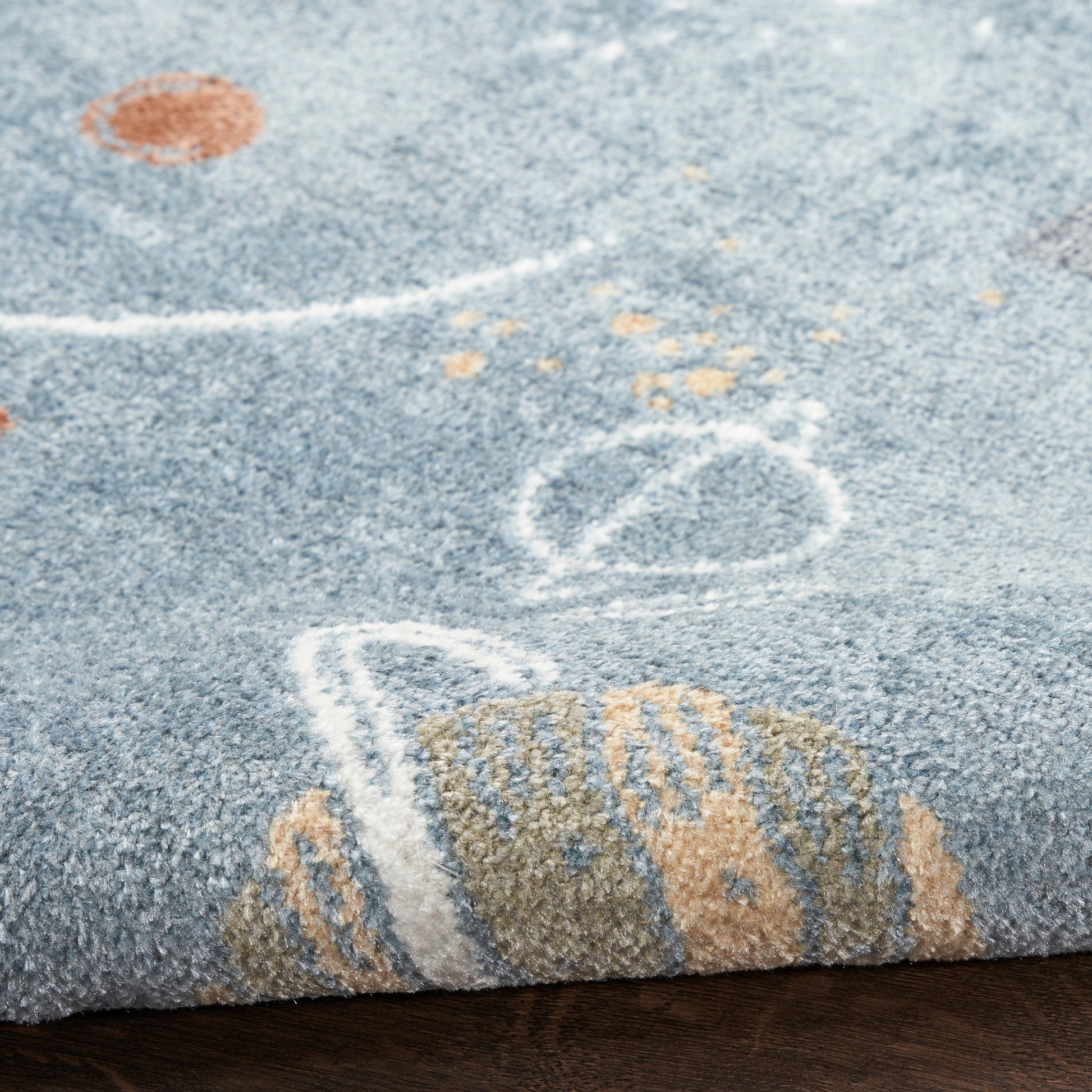 Close-up of blue textured rug with soft pile, white chalk-like lines and orange accents on a wooden floor edge.