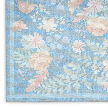 Blue floral rug with pastel pink and white flowers, green leaves, woven texture, corner view.