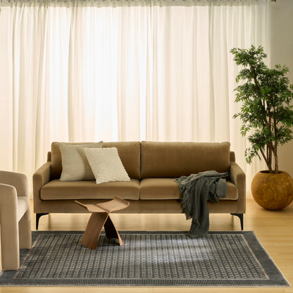 Beige fabric sofa with textured white pillows, gray throw, wooden sculptural coffee table, blue-gray rug, potted plant.