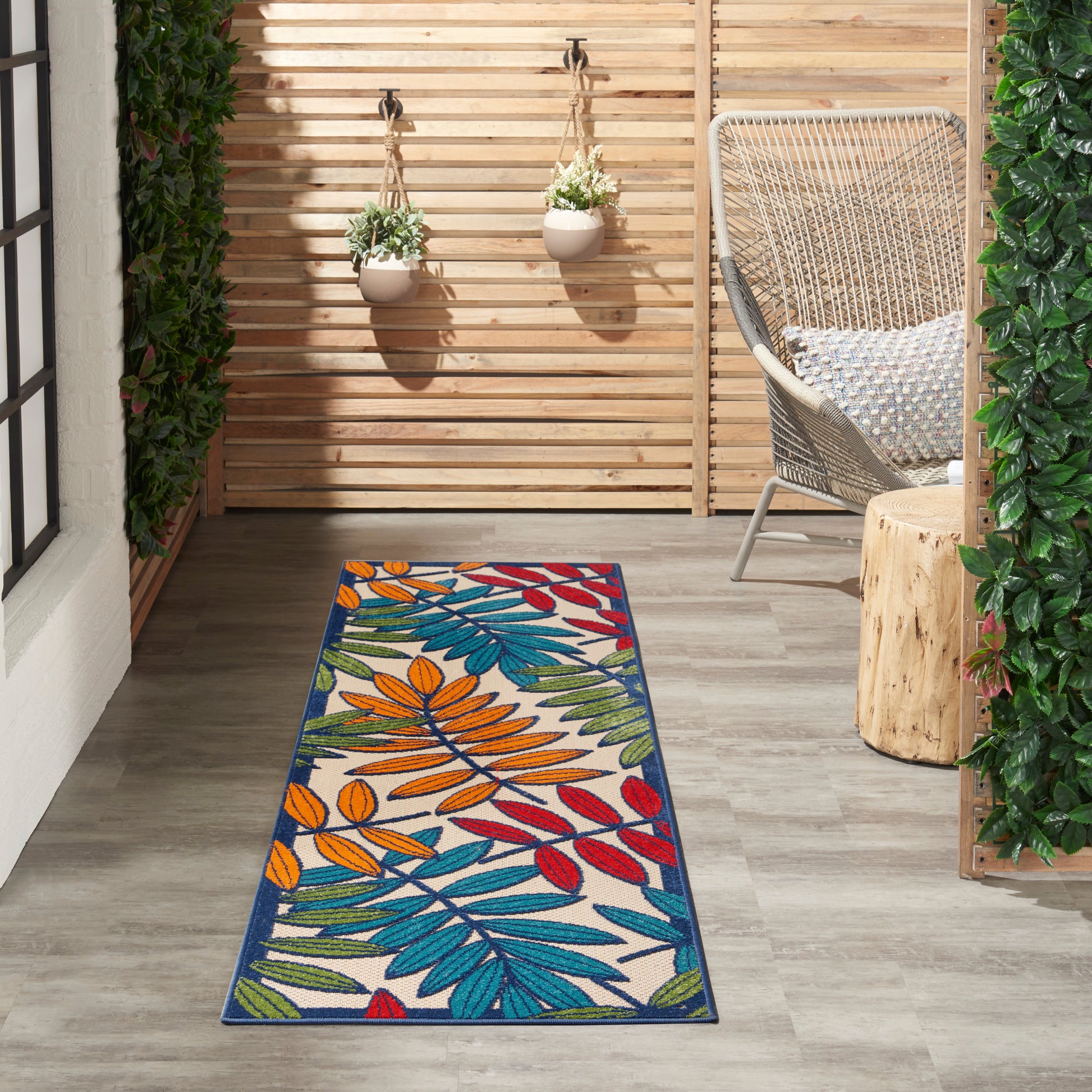 Outdoor patio runner rug with tropical leaf pattern in blue, orange, red, teal on white; blue border beside wicker chair