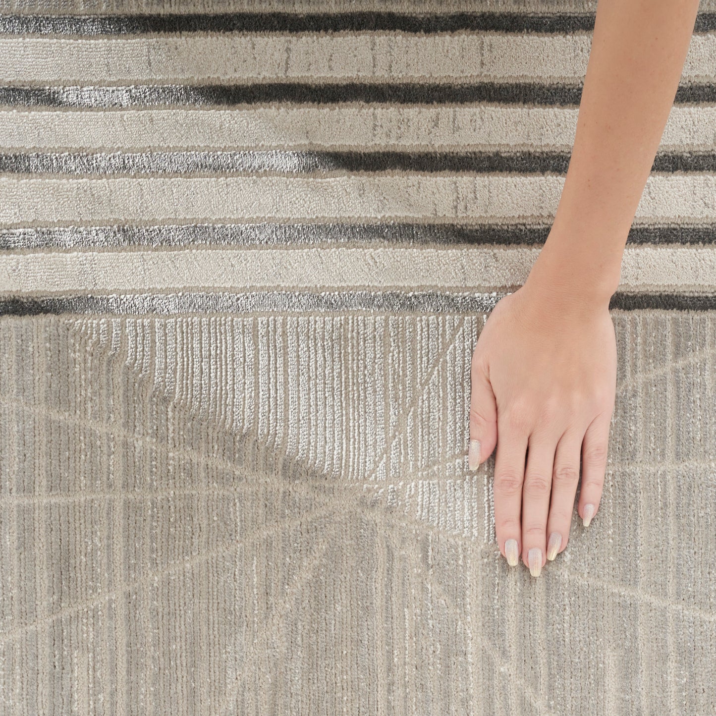 Beige textured rug with subtle geometric lines; 5' x 7' size; hand resting on surface for scale; neutral, modern style.