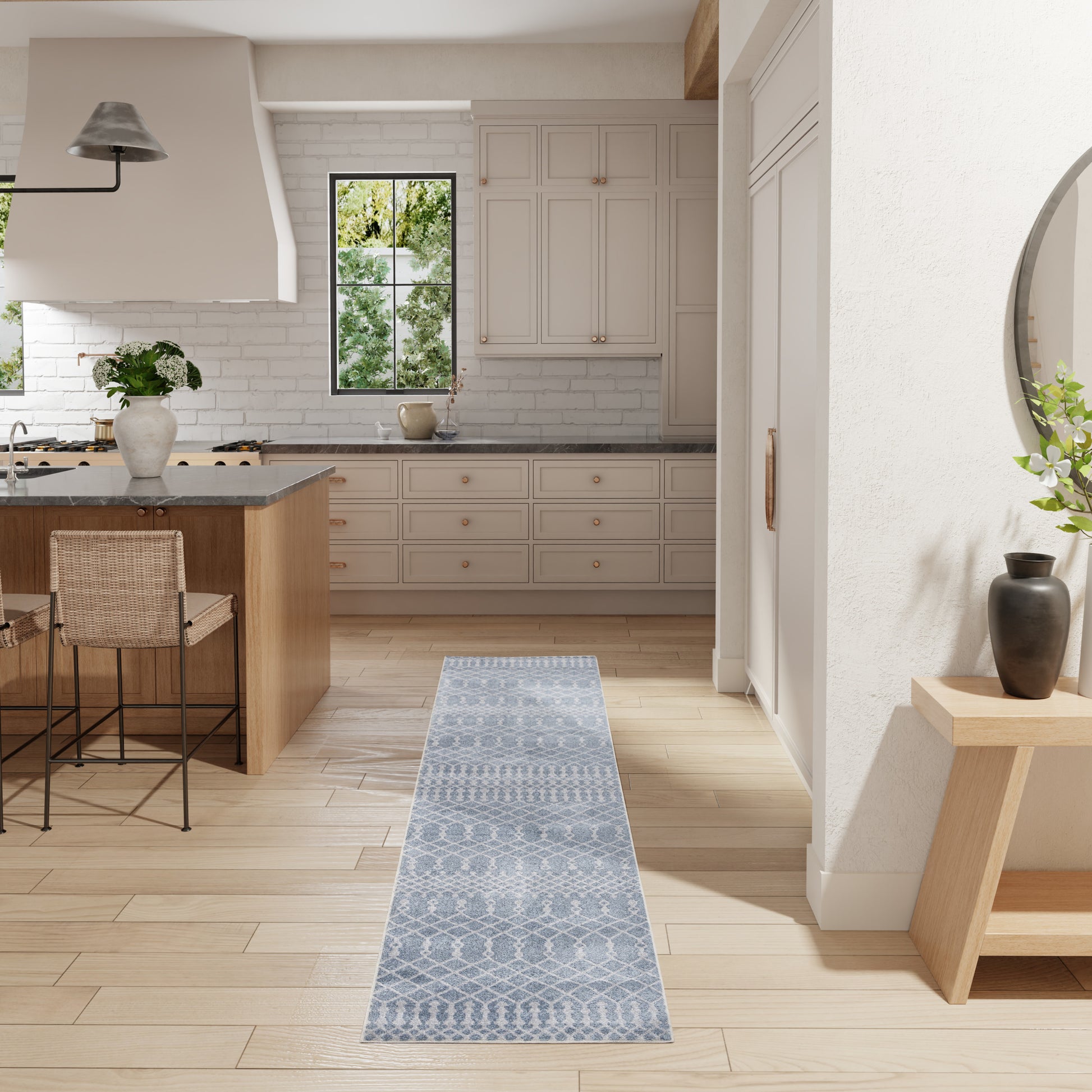 Blue-gray woven geometric runner rug on light wood floor in a bright white kitchen with an island and stools.