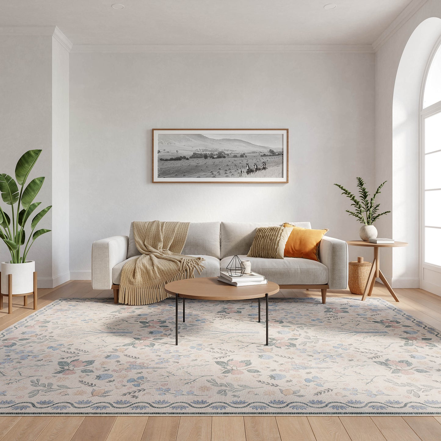 Bright living room with gray sofa, beige throw and orange cushion, round coffee table, patterned rug, green plants, window