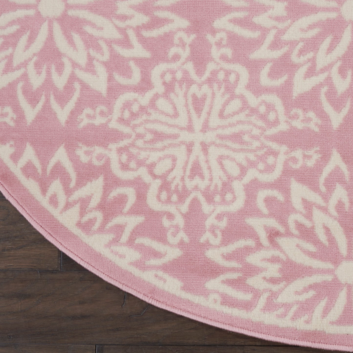 Round pink rug with a white mandala-style floral pattern on dark wood floor.