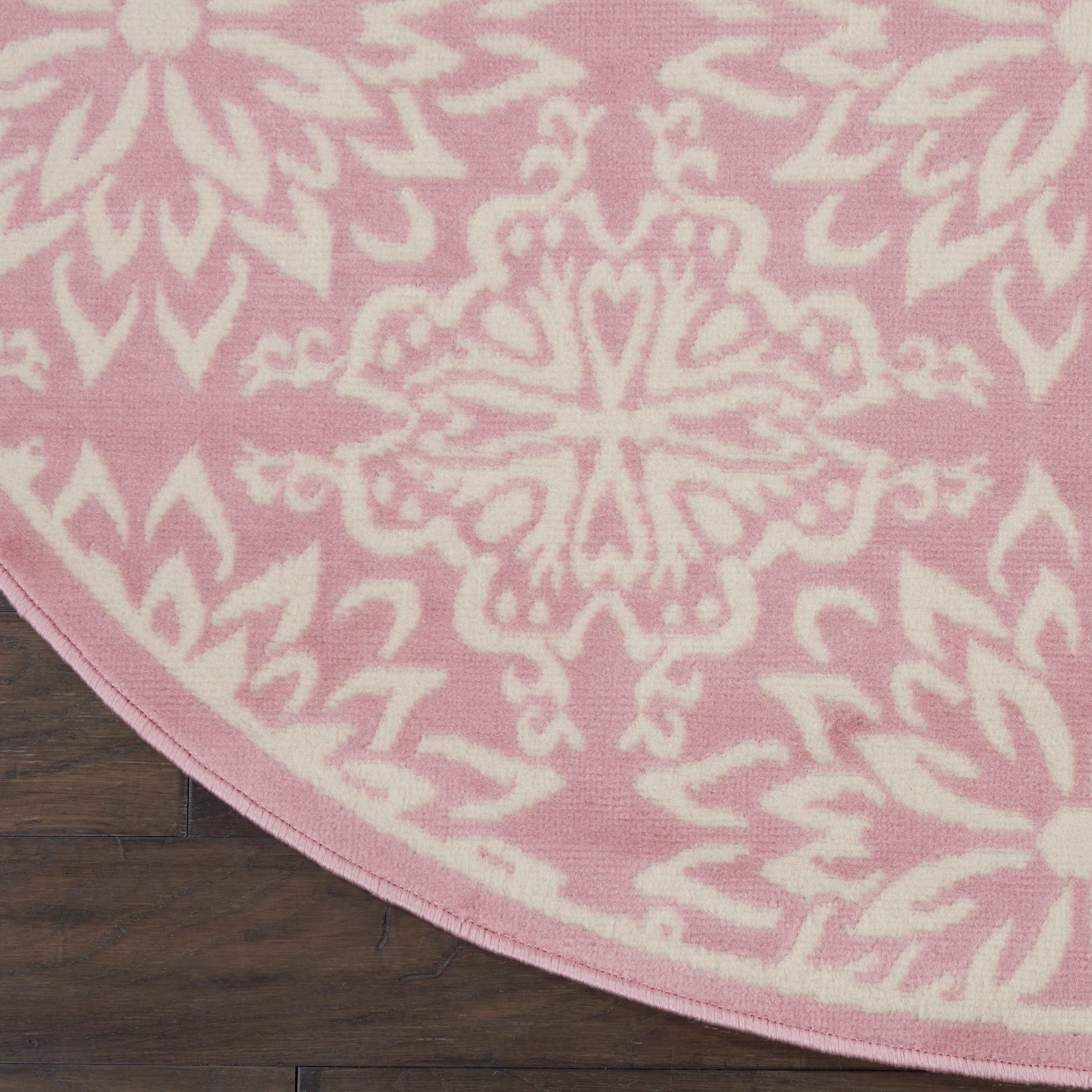 Round pink rug with a white mandala-style floral pattern on dark wood floor.