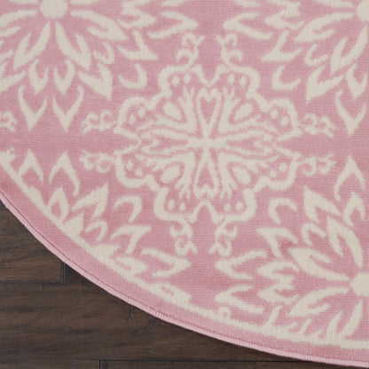 Round pink rug with a white mandala-style floral pattern on dark wood floor.
