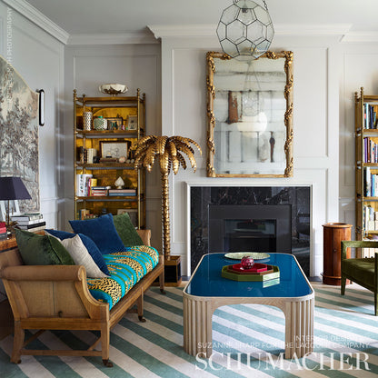 Gold palm tree sculpture beside a blue glass-top coffee table in a gray-paneled living room with striped rug.