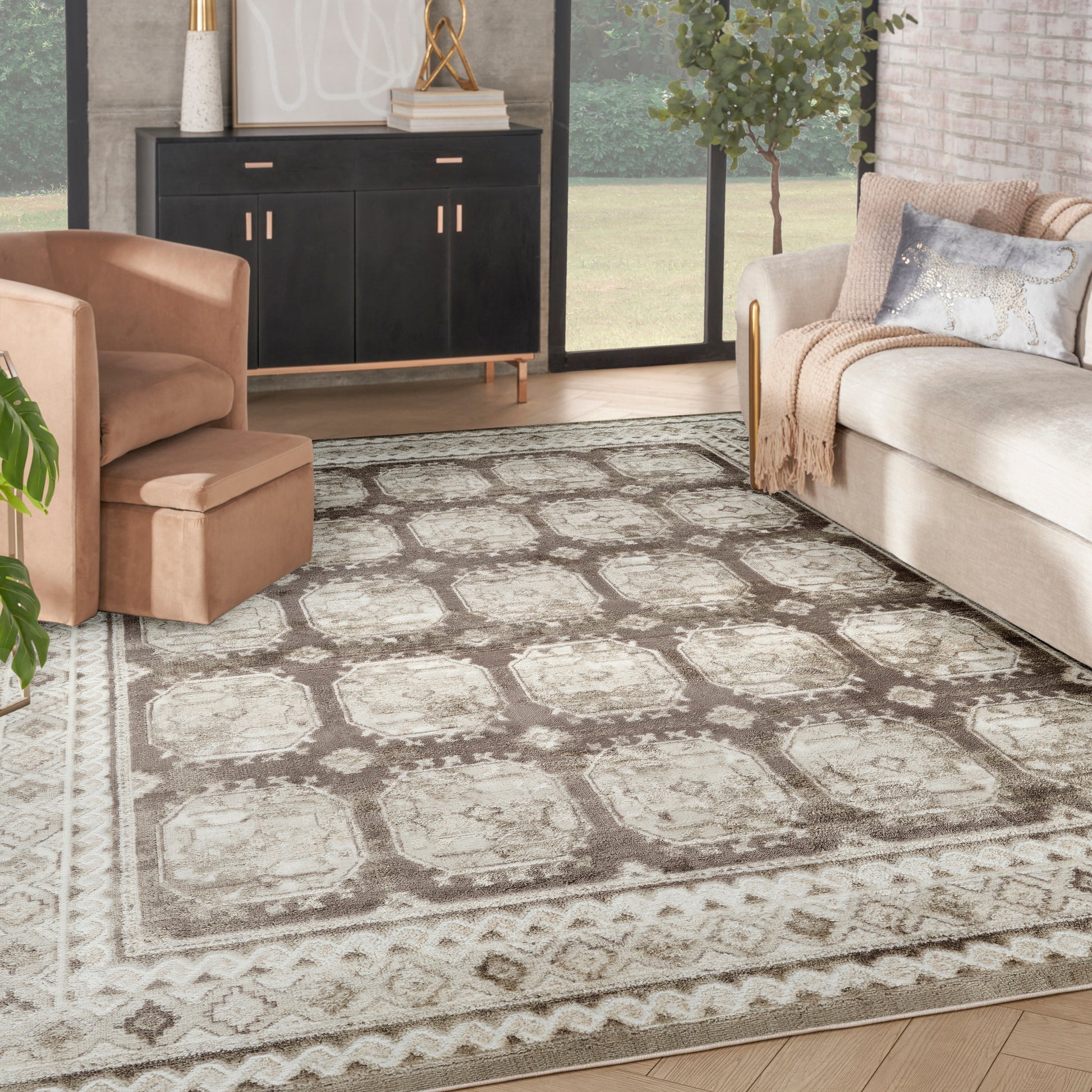 Beige-gray patterned area rug anchors a modern living room with tan chair, light sofa, black credenza, and big windows.