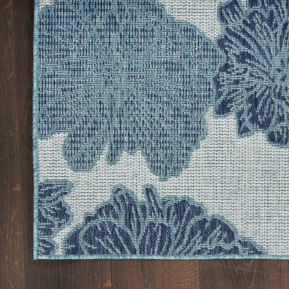 Blue floral woven rug with teal border on ivory background, laid on dark wood floor.