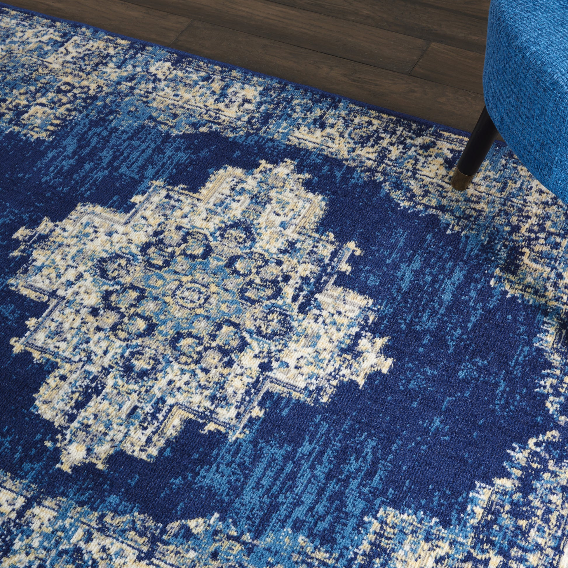 Blue distressed oriental rug with ivory central medallion on dark wood floor; blue sofa leg visible.