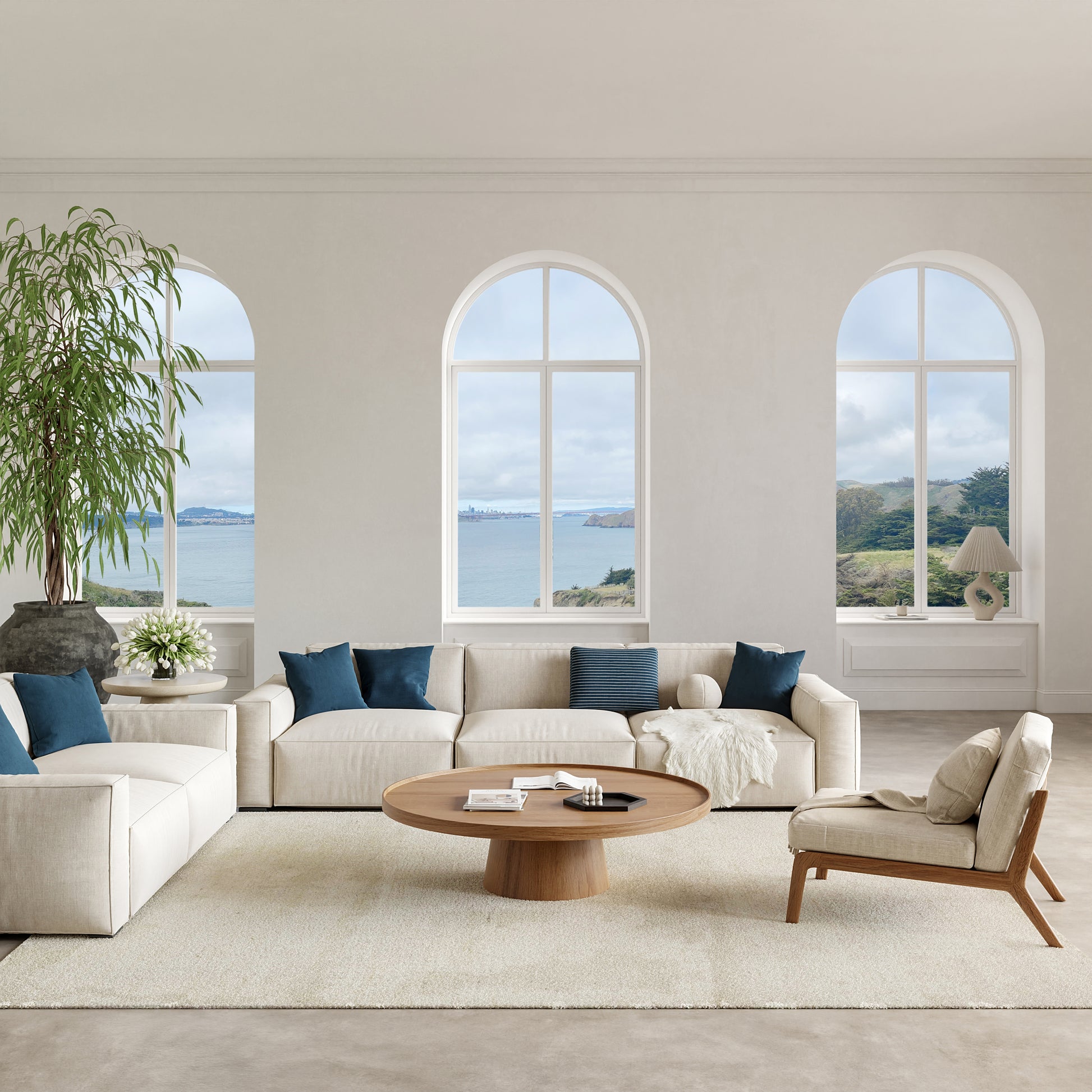 Coastal living room with cream sectional, blue cushions, beige armchair, round wood coffee table, arched ocean-view windows.