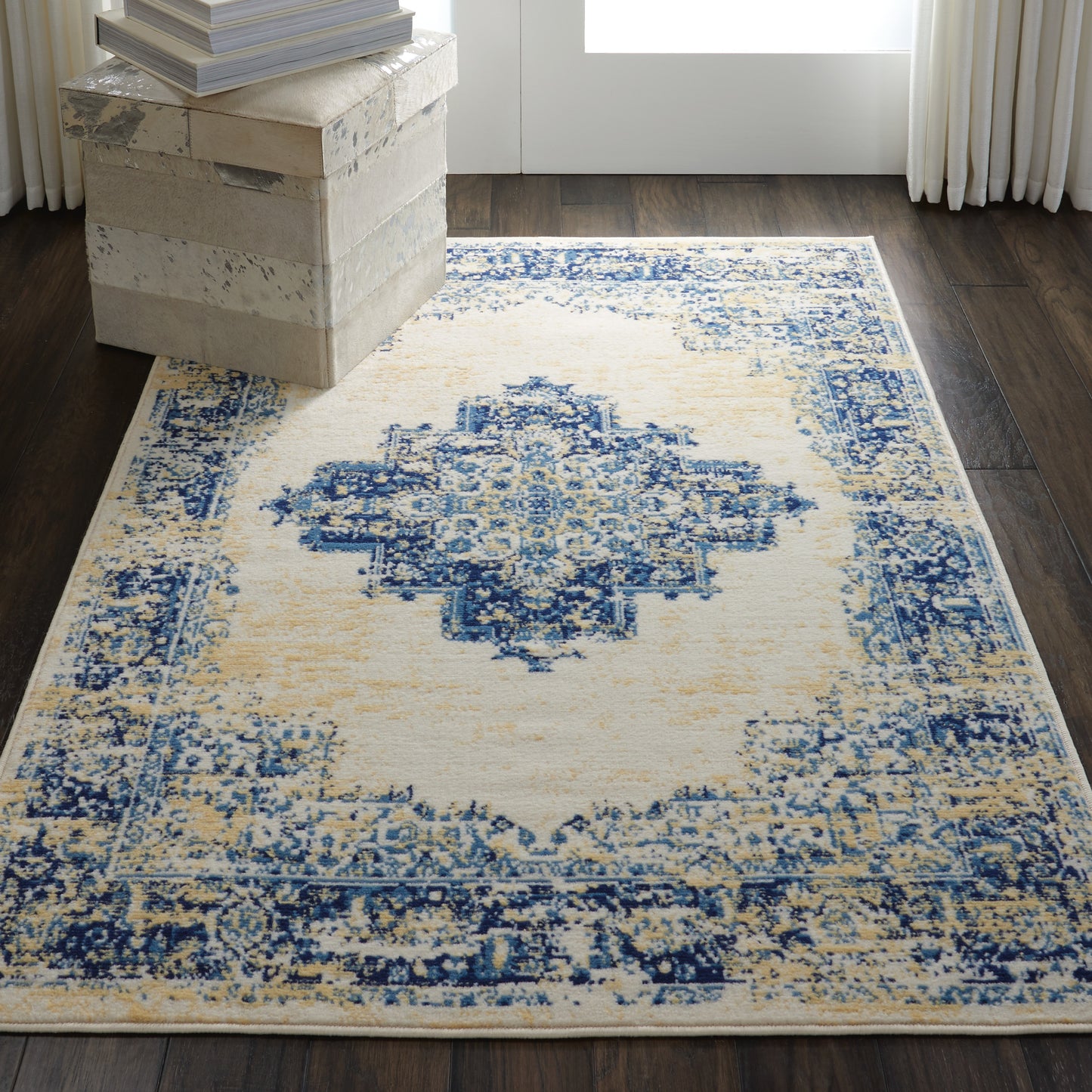 Rectangular distressed blue and ivory oriental area rug with central medallion, on dark wood floor, in a living room scene.