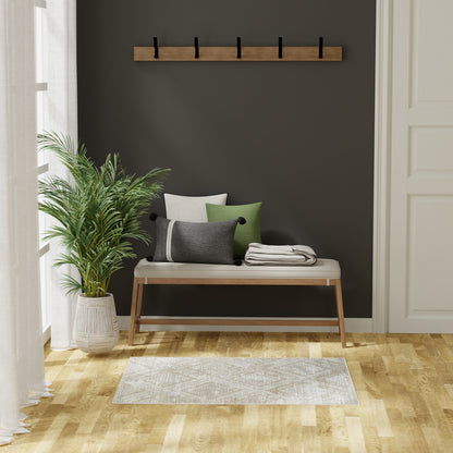 2' x 4' light rug on floor in a room with a wood bench, beige cushion, green/gray/white pillows, folded throw; dark wall, wood coat rack, potted plant.