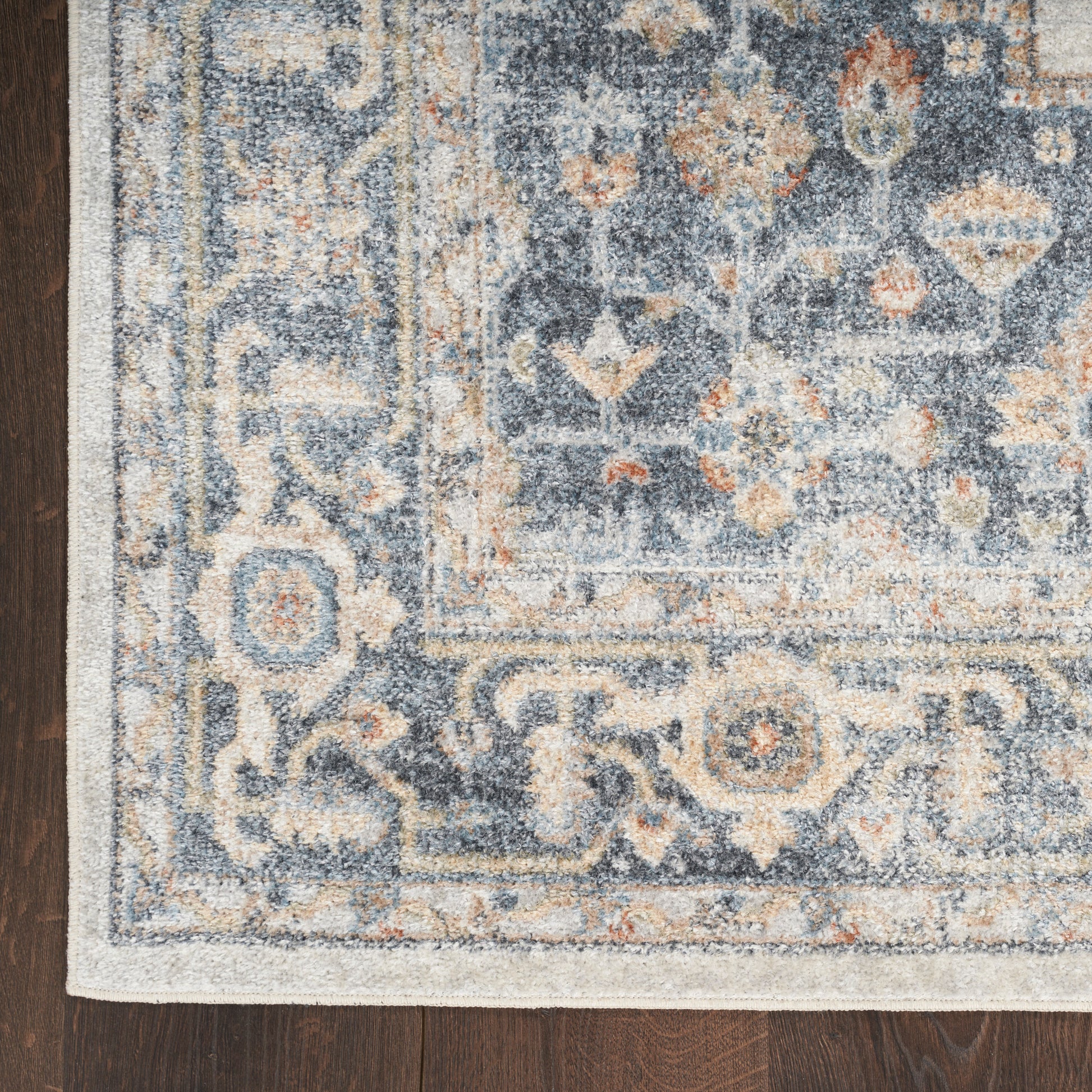 Rectangular blue-gray traditional rug with ivory, beige, and orange floral motifs and an ornate border on a dark wood floor.