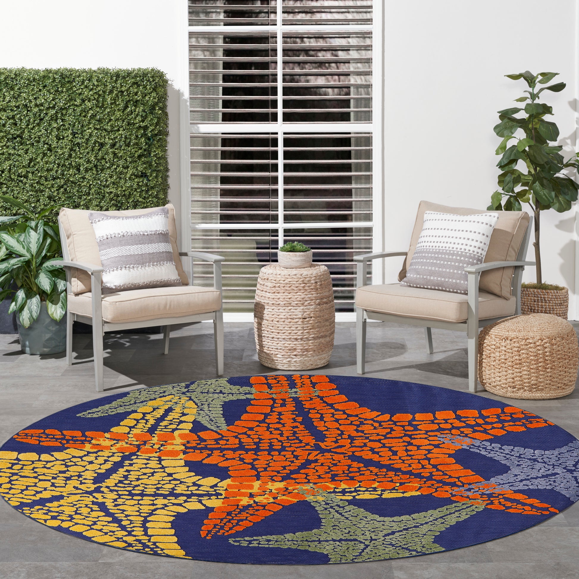 Circular outdoor rug with orange starfish on navy blue; yellow and green accents; two beige patio chairs nearby.