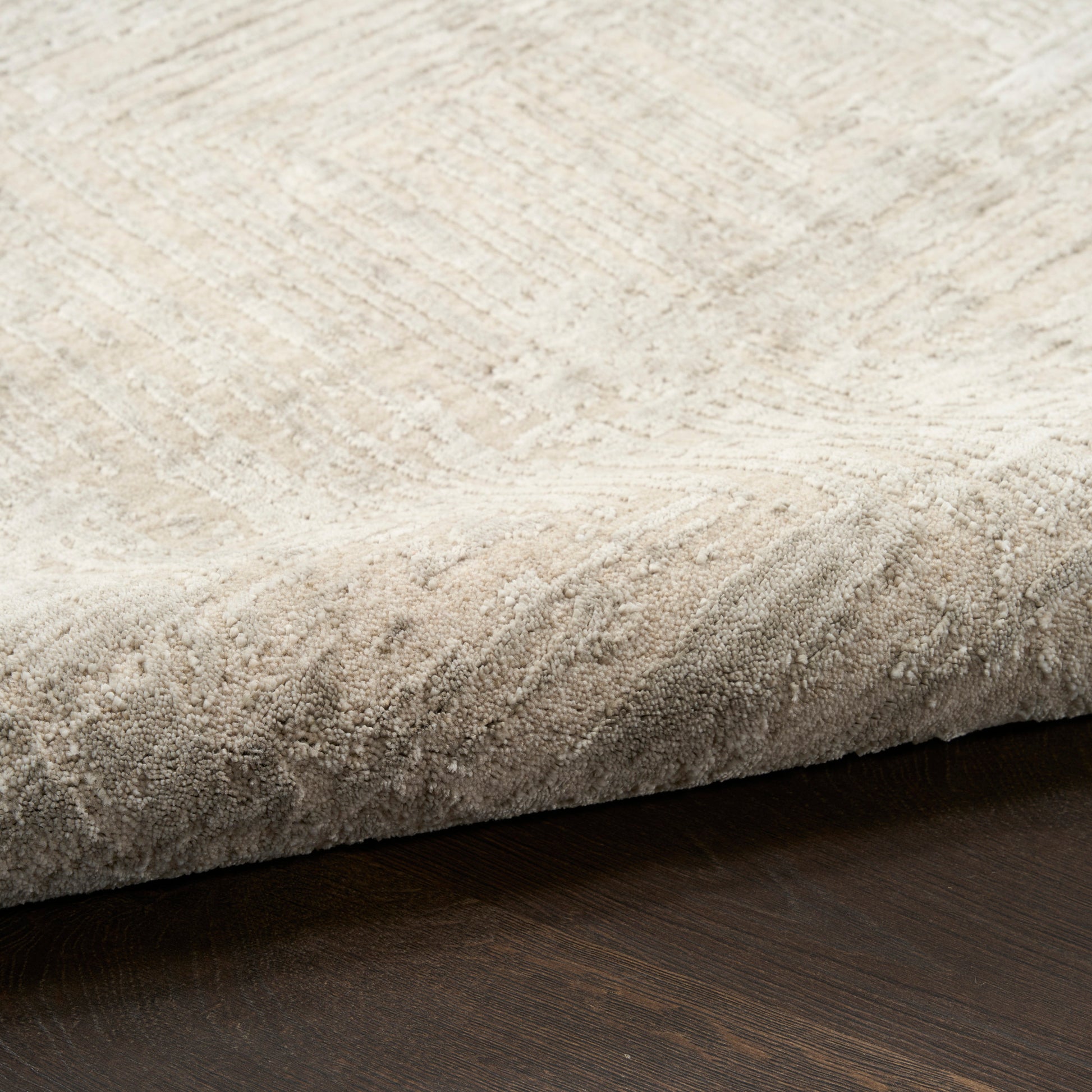 Beige textured pile rug with a subtle banded pattern and curled edge on dark wood floor.