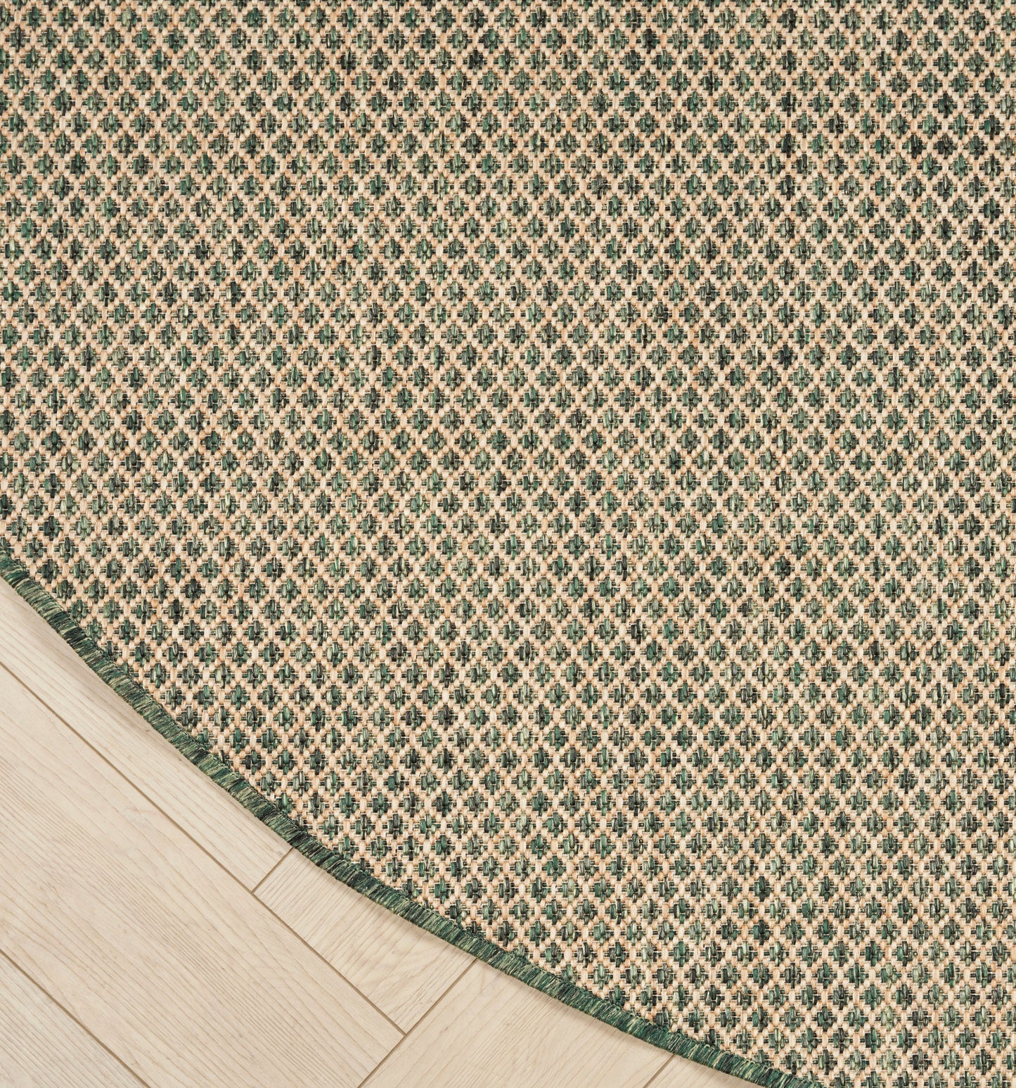 Round woven rug with green border and tiny diamond lattice pattern on light wood floor.