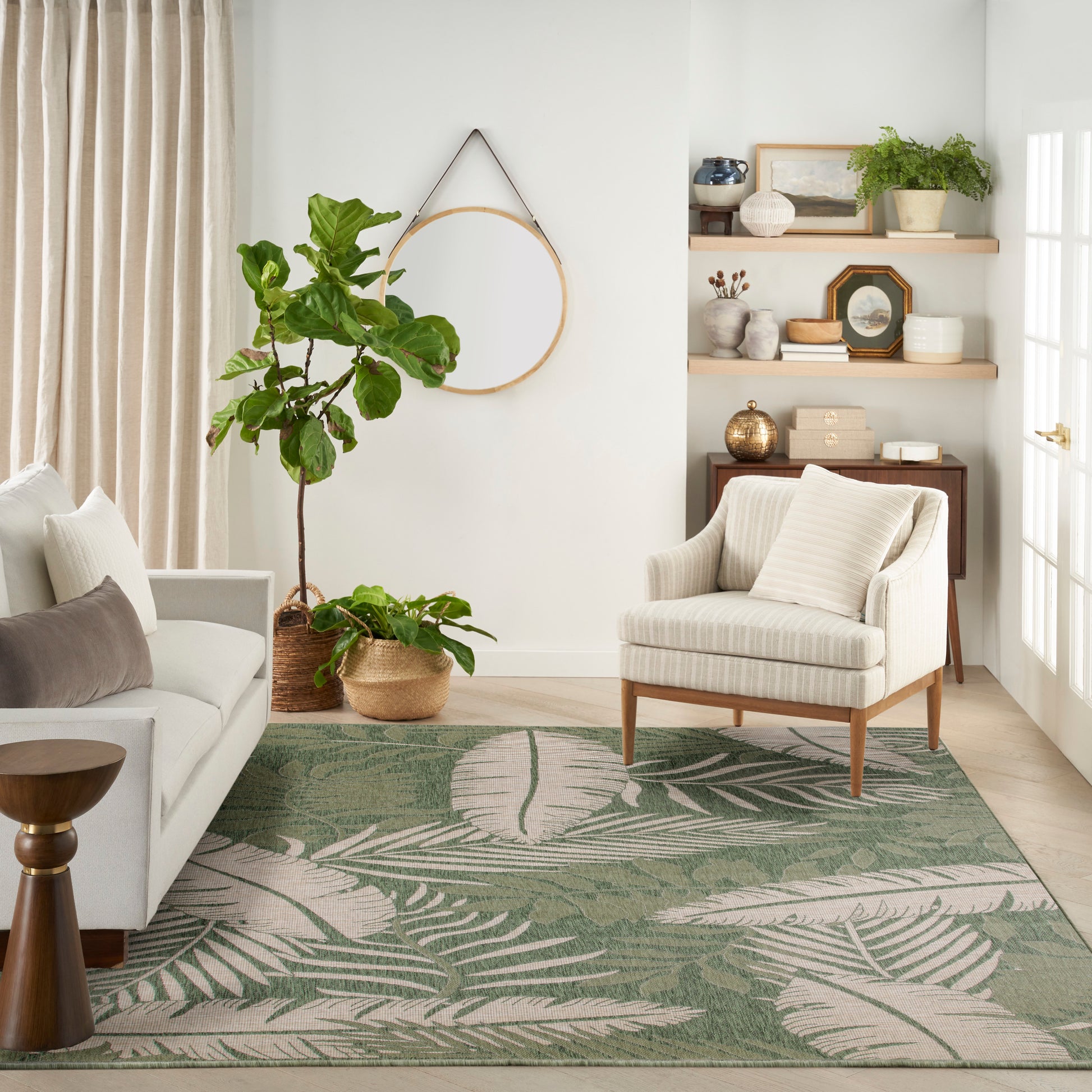 Living room with green palm-leaf rug, cream sofa and striped armchair, indoor plant, woven baskets, round hoop mirror.