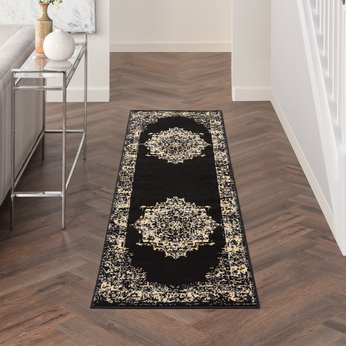 Black hallway runner rug with cream ornate medallions and a decorative border in a modern entryway beside a metal console.