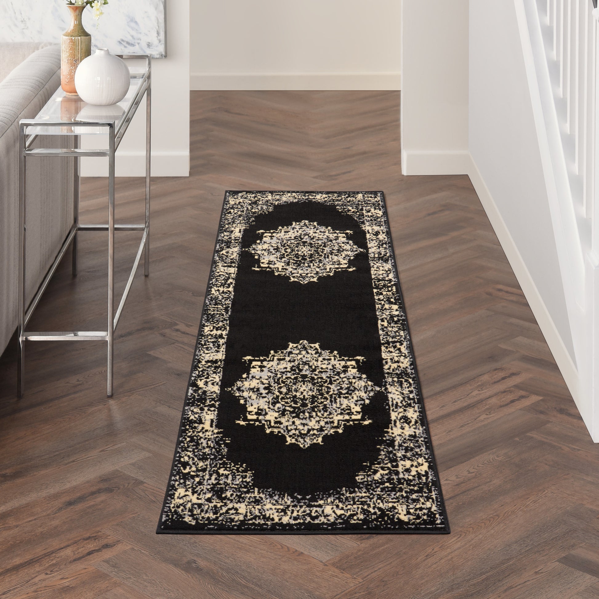 Black hallway runner rug with cream ornate medallions and a decorative border in a modern entryway beside a metal console.