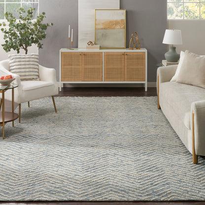 Bright living room with blue chevron rug, ivory sofa and armchair, white console with six woven rattan panels, greenery.