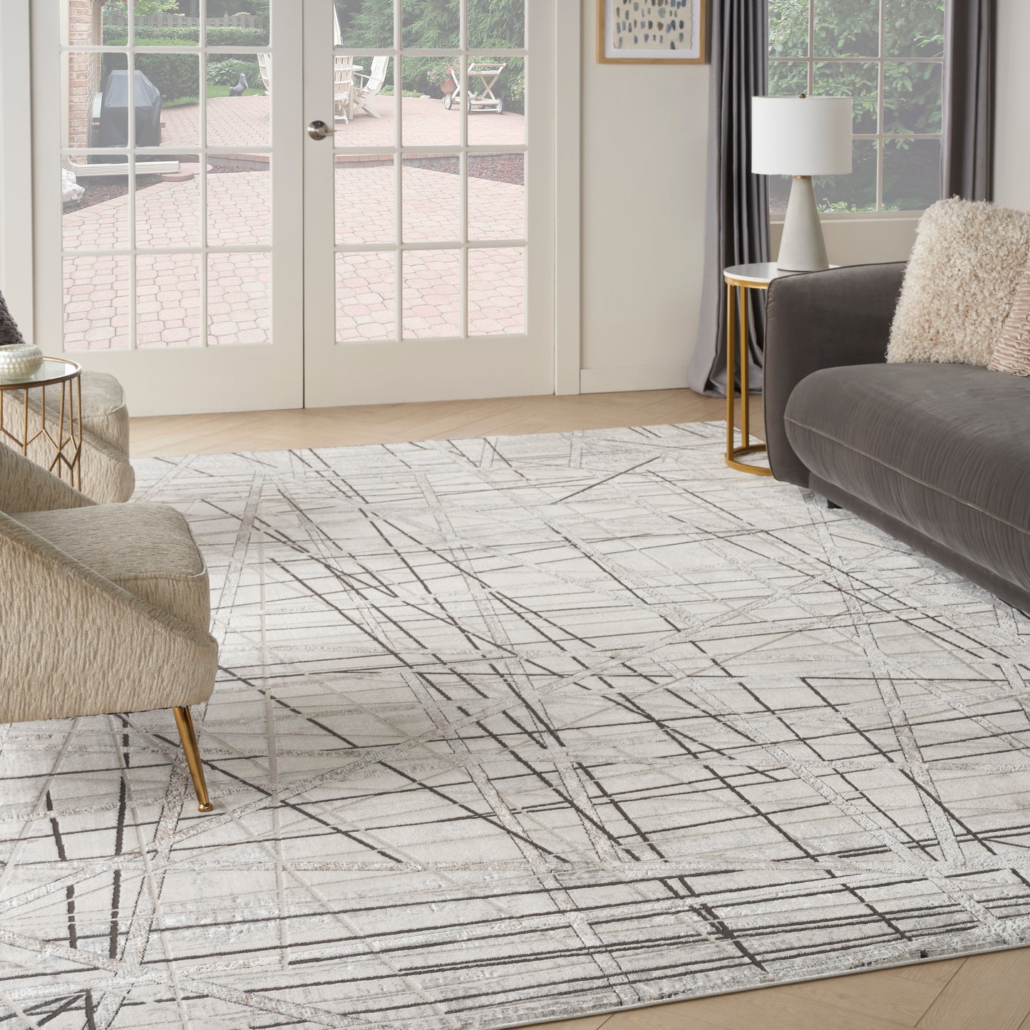 Cream area rug with black linear geometric pattern in a modern living room; beige boucle chair, gray sofa, gold tables.