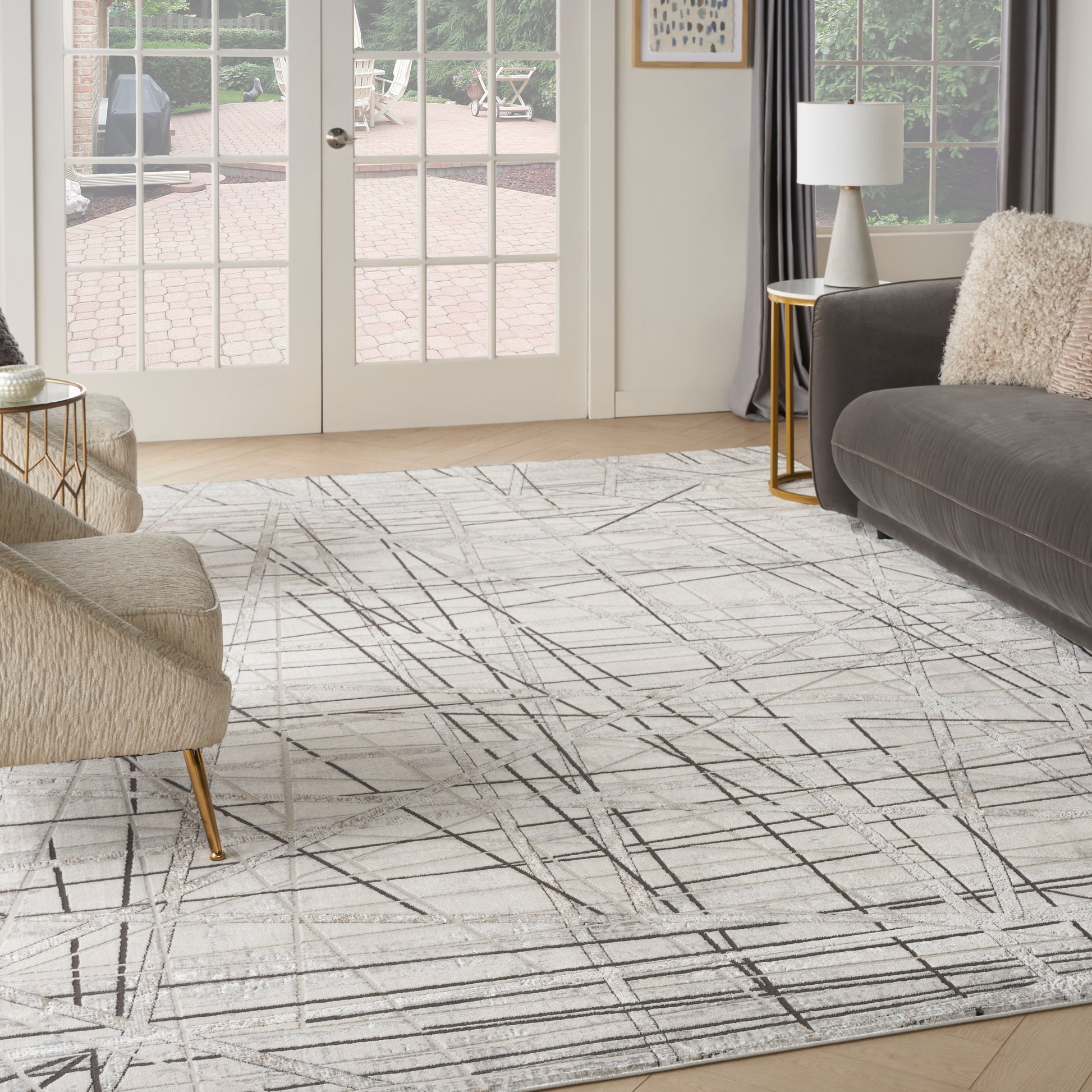 Cream area rug with black linear geometric pattern in a modern living room; beige boucle chair, gray sofa, gold tables.