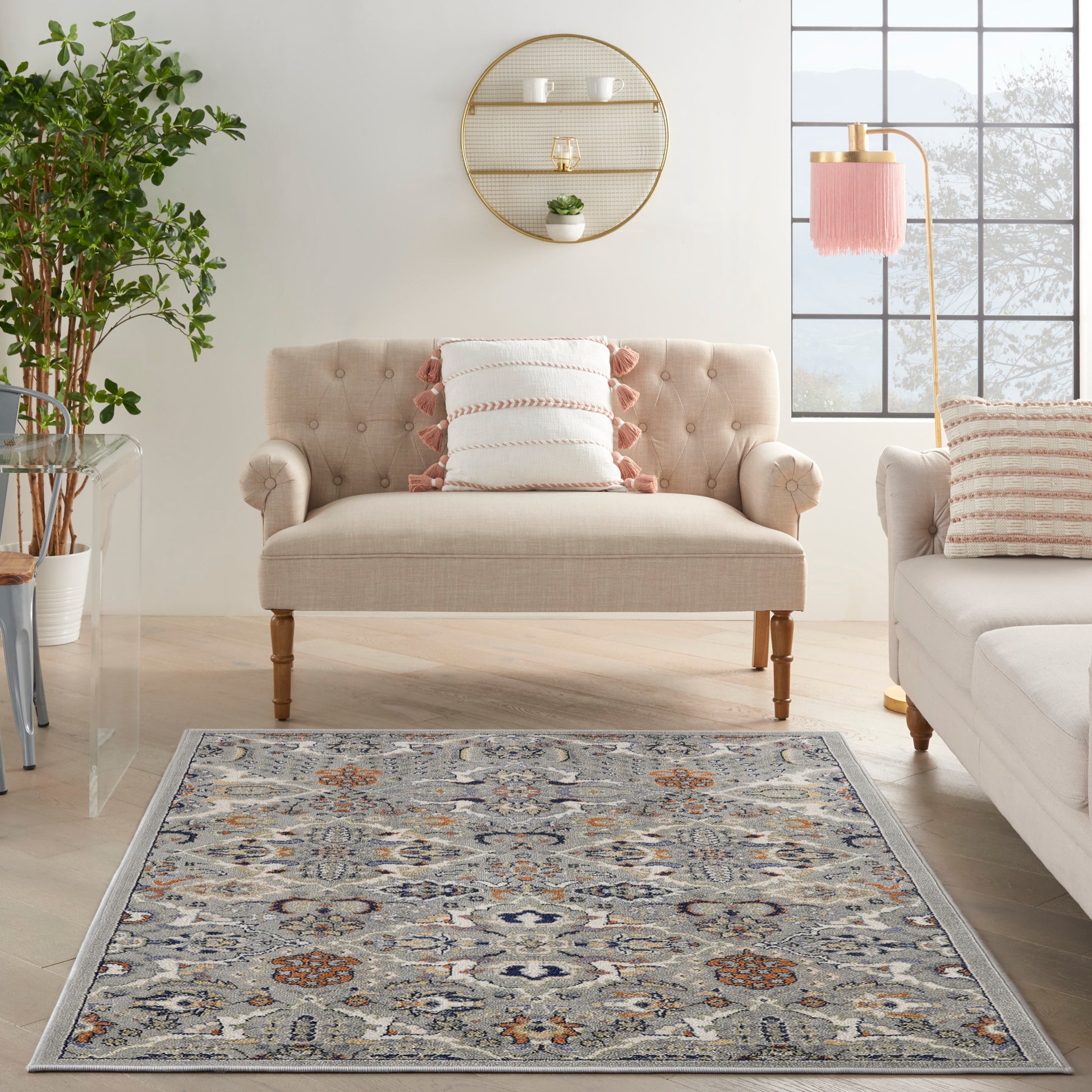 Beige tufted loveseat with rolled arms and wooden legs in a bright living room with a blue-gray rug and orange accents.