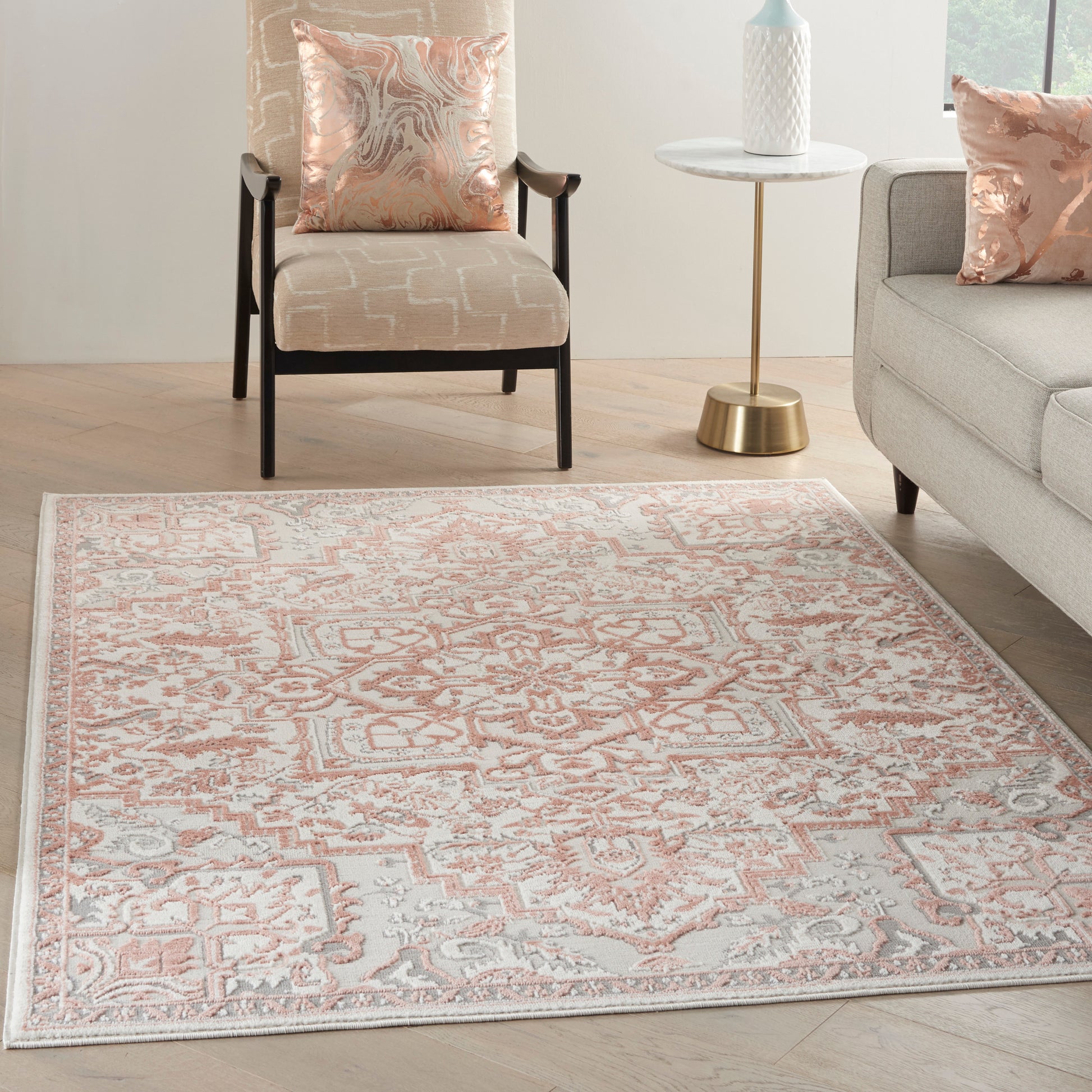 Peach and ivory oriental-pattern area rug on light wood floor, paired with beige chair, gray sofa, and blush cushions.